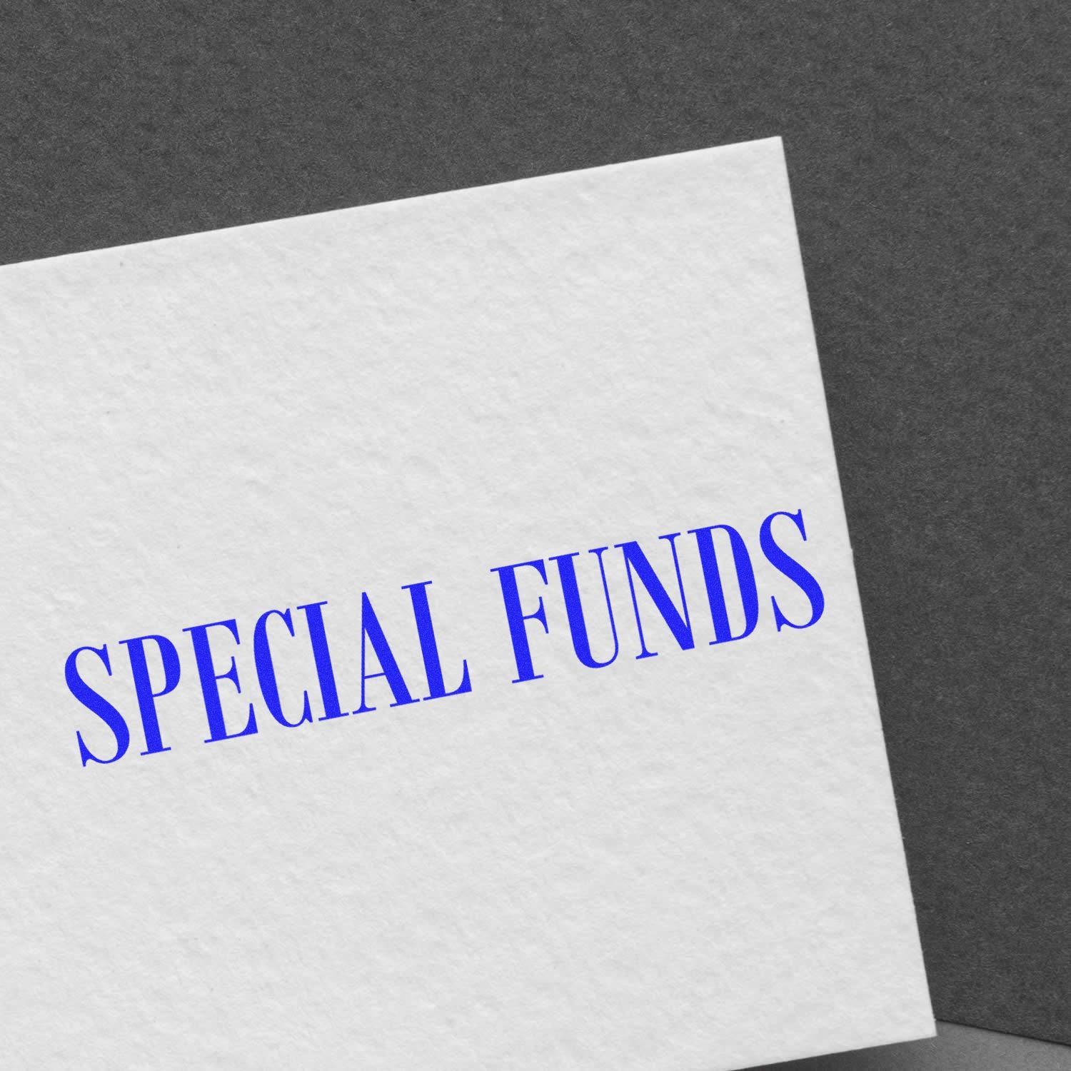 White paper stamped with blue 'SPECIAL FUNDS' text using the Large Self Inking Special Funds Stamp, placed on a dark gray background.