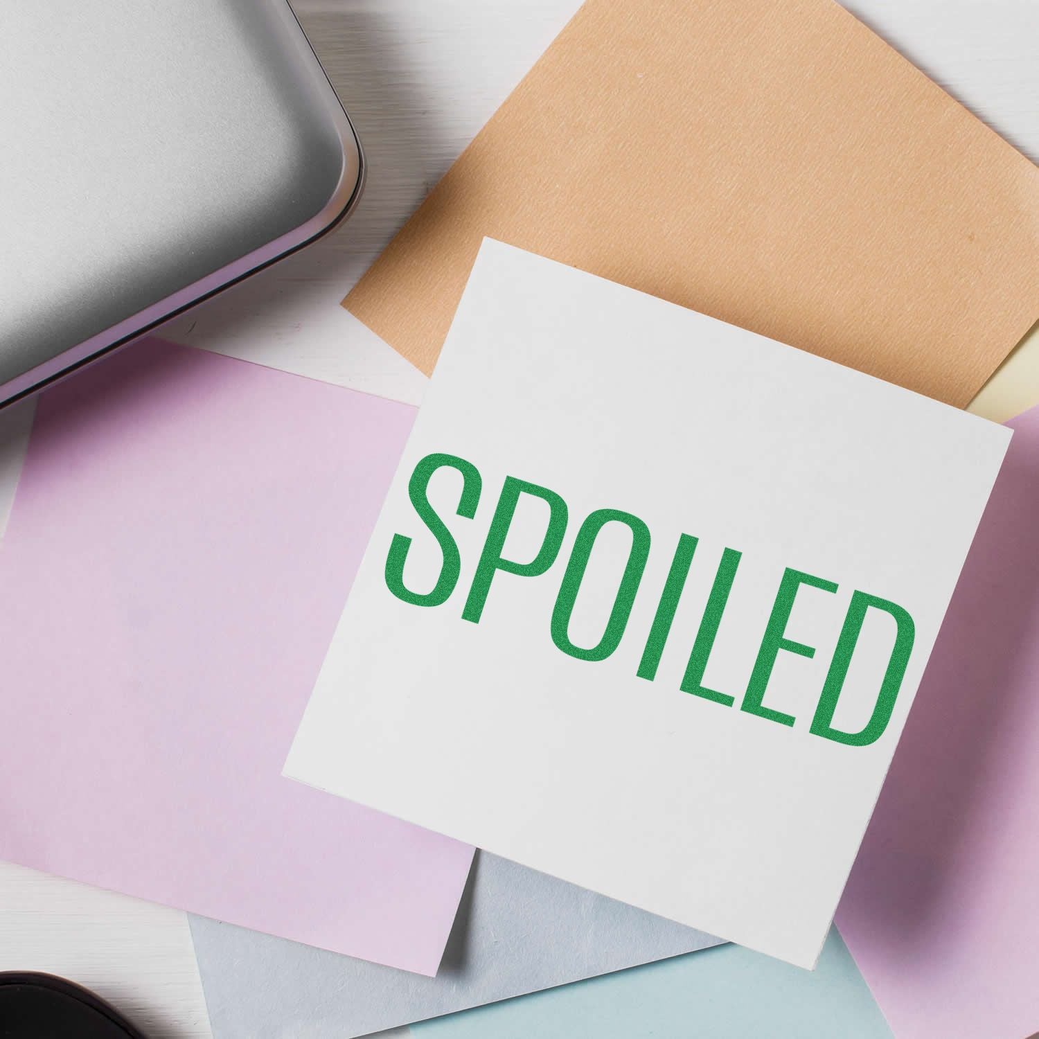 Self Inking Spoiled Stamp in use on a white card surrounded by pastel-colored papers and a silver laptop.