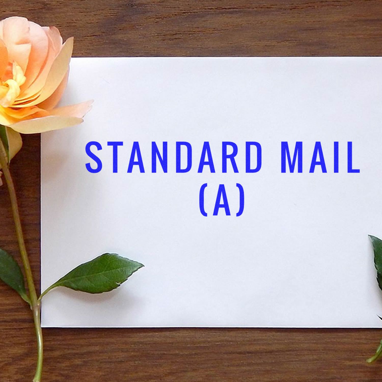 Standard Mail (A) Rubber Stamp impression on a white envelope placed on a wooden surface with a yellow rose on the side.