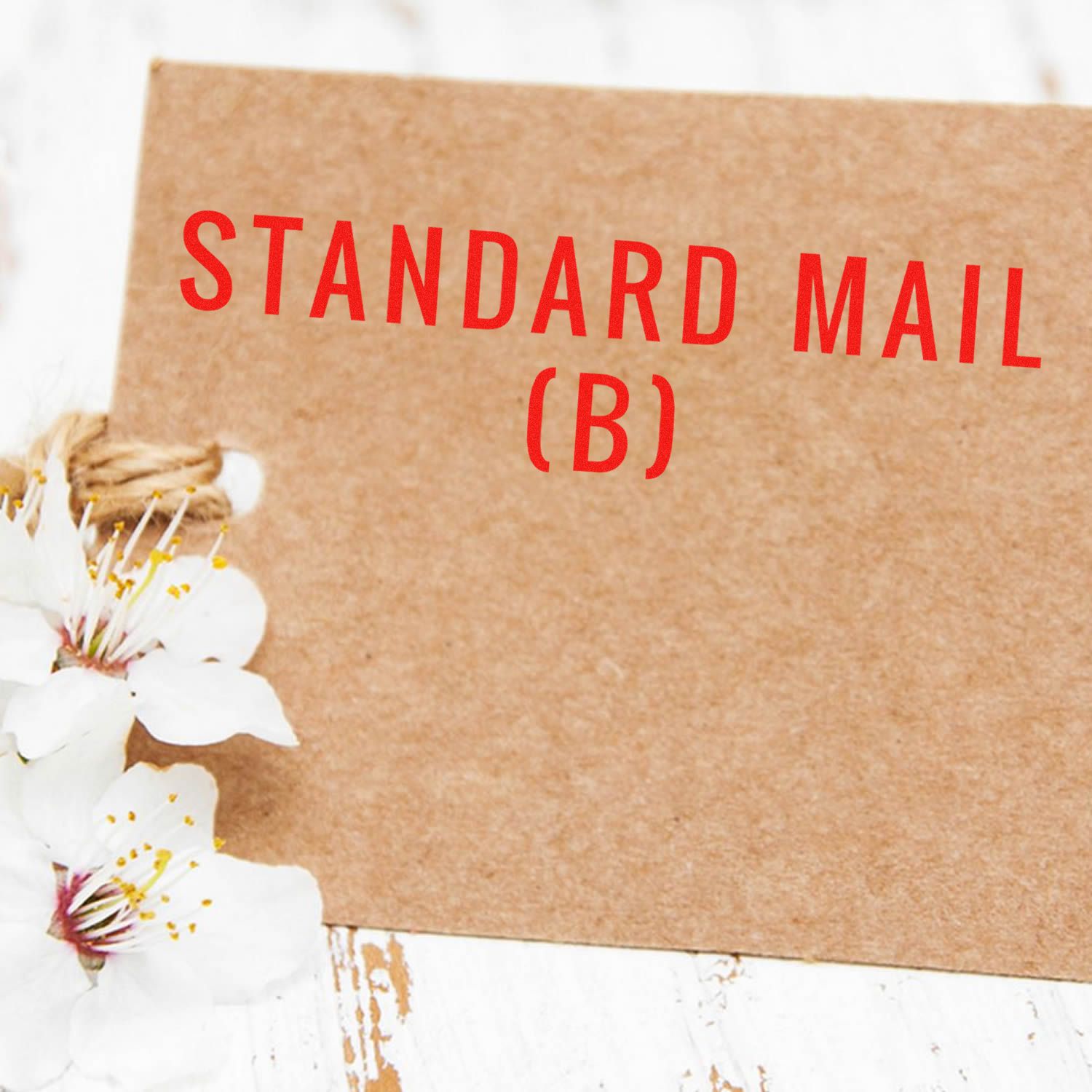 Large Self Inking Standard Mail (B) Stamp used on a brown envelope with white flowers on a rustic white wooden surface.