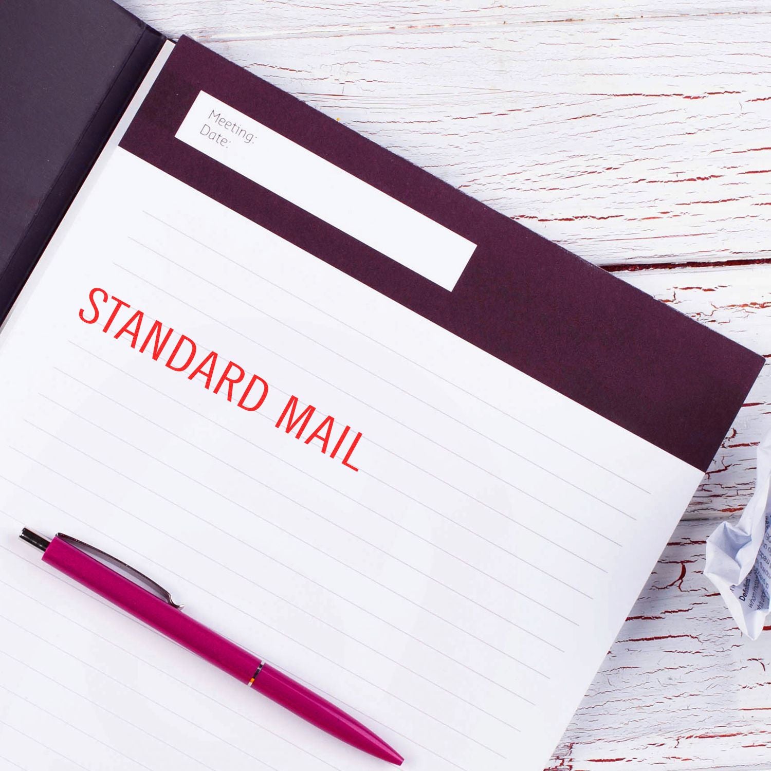 Slim Pre-Inked Standard Mail Stamp in red ink on a notebook page with a purple pen beside it on a white wooden table.