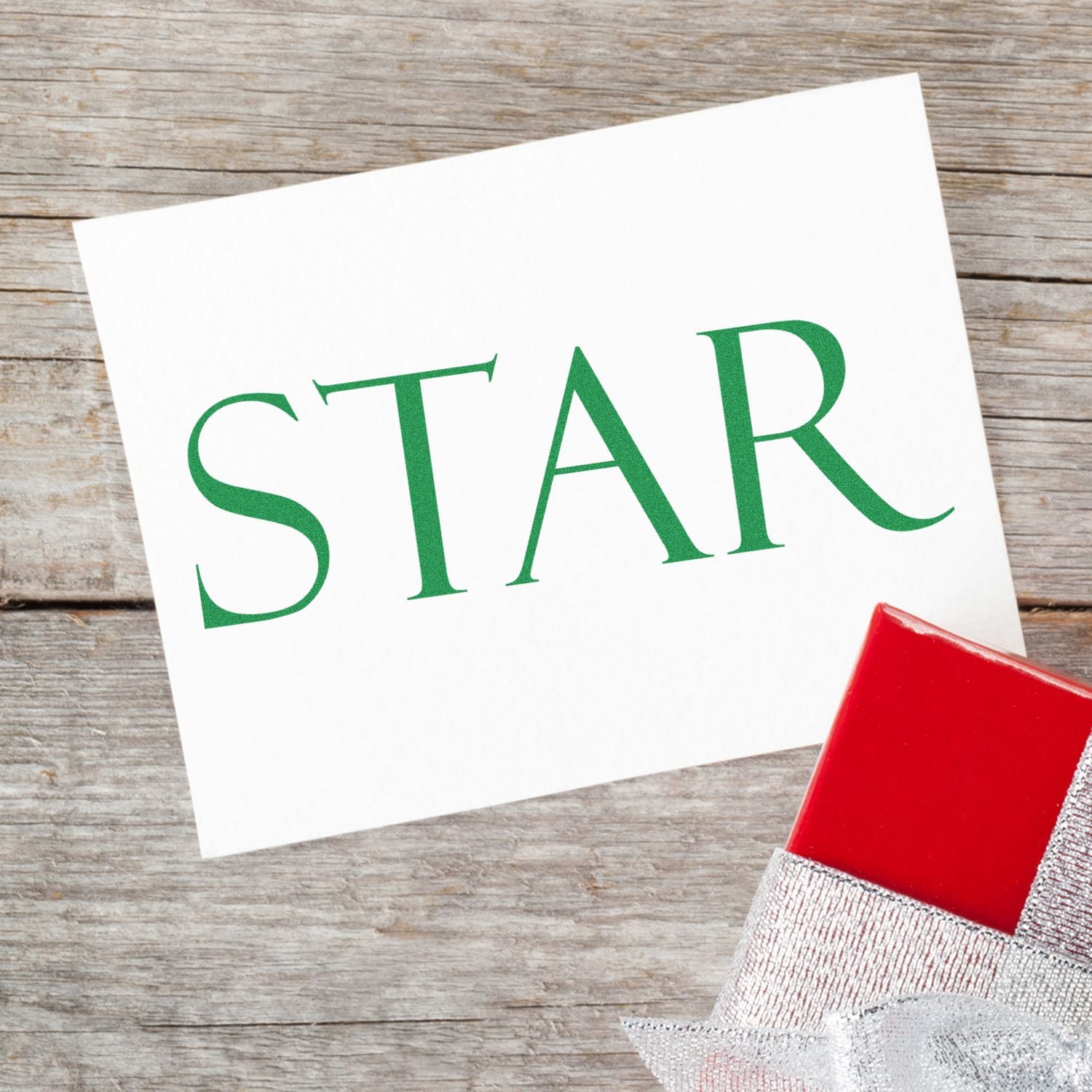 Large Self Inking Star Stamp used on a white card with STAR in green letters, placed on a wooden surface next to a red gift box.