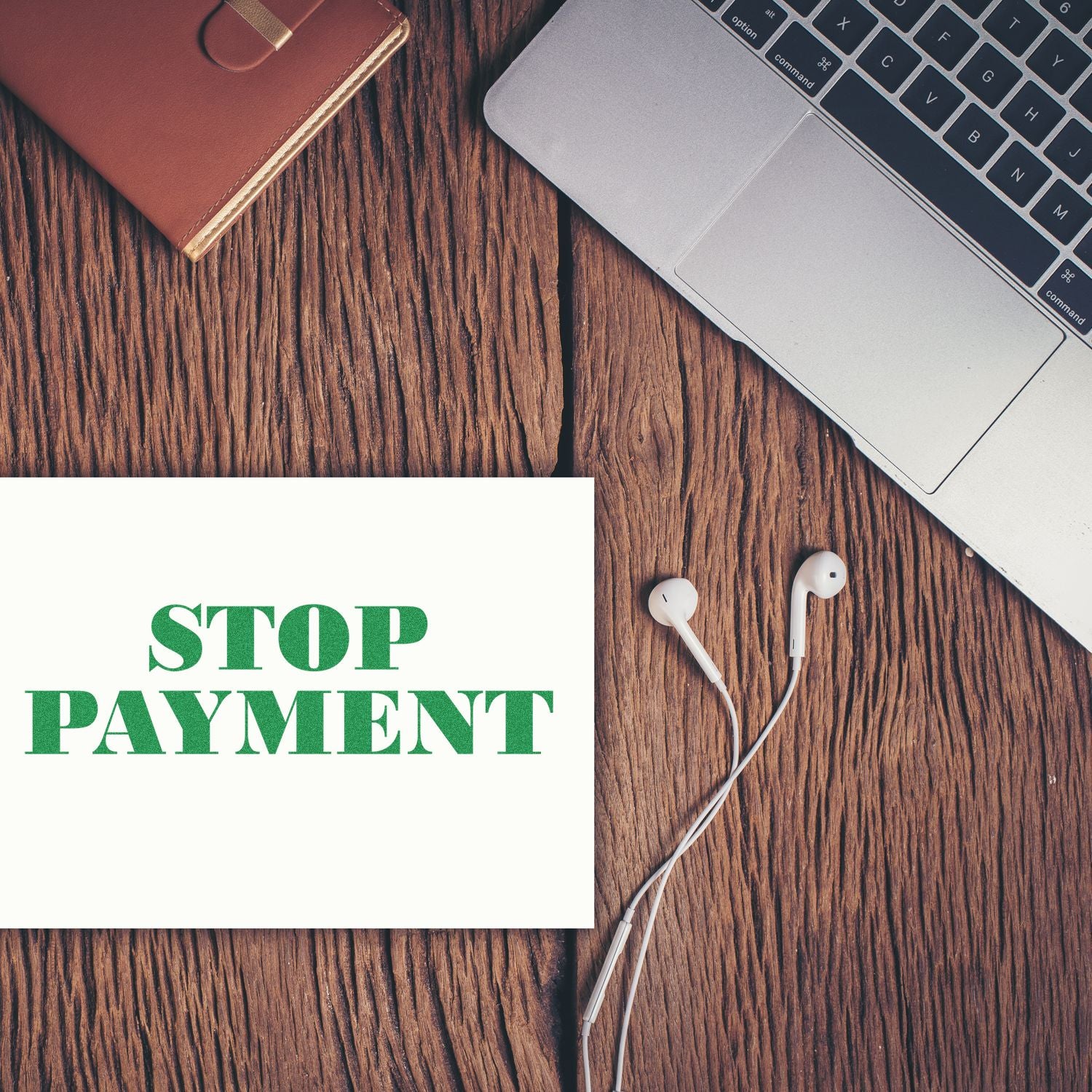 Self Inking Stop Payment Stamp on a white paper beside a laptop, earphones, and a brown notebook on a wooden surface.