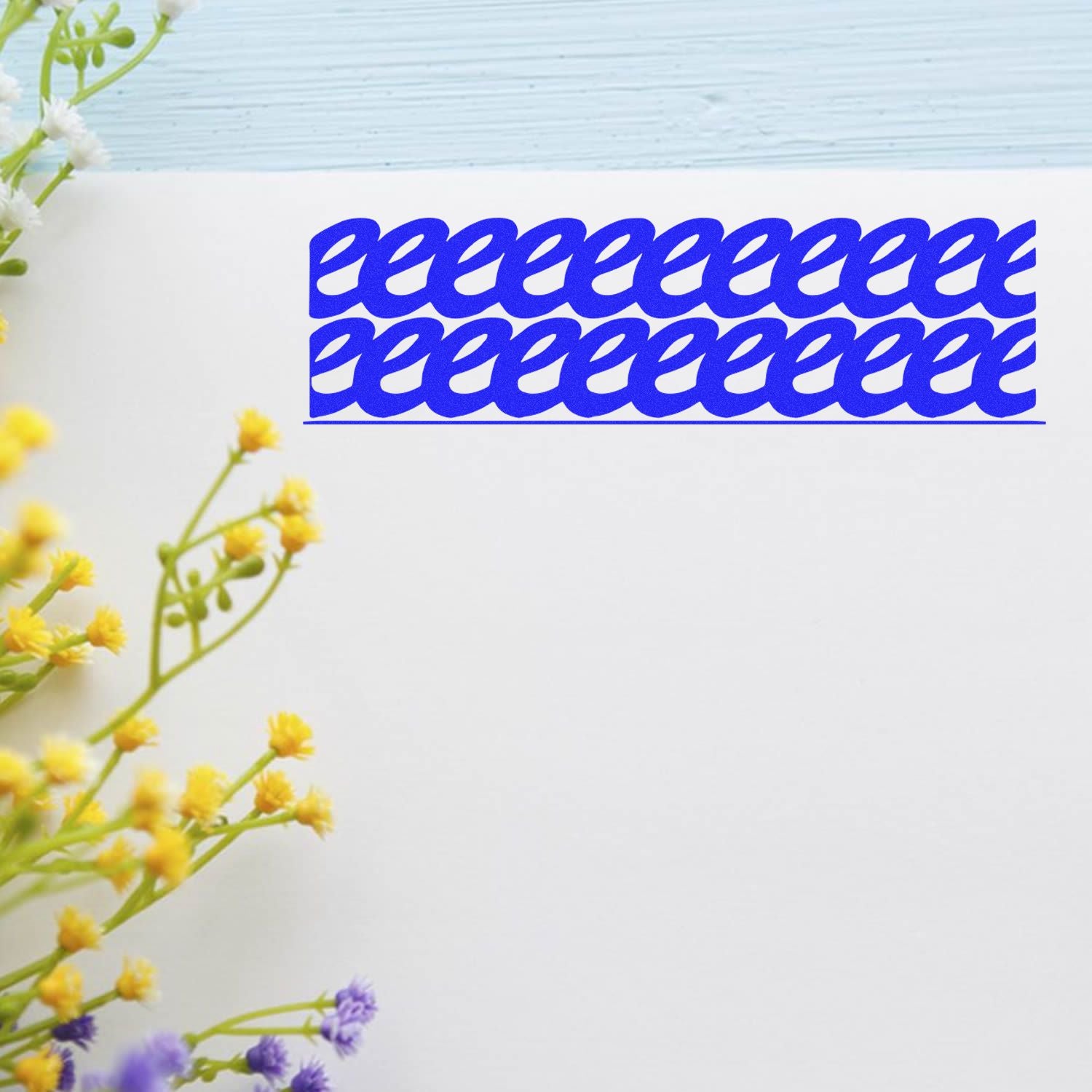 Strikeout Rubber Stamp in blue ink creating a repeated pattern on white paper, with yellow and purple flowers on the side.