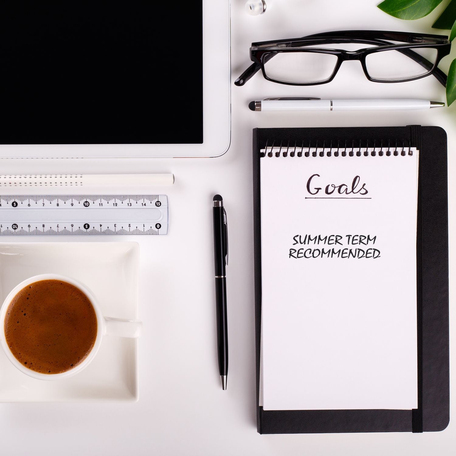 Desk with a cup of coffee, tablet, glasses, ruler, pen, and notebook stamped with Self Inking Summer Term Recommended Stamp under Goals .