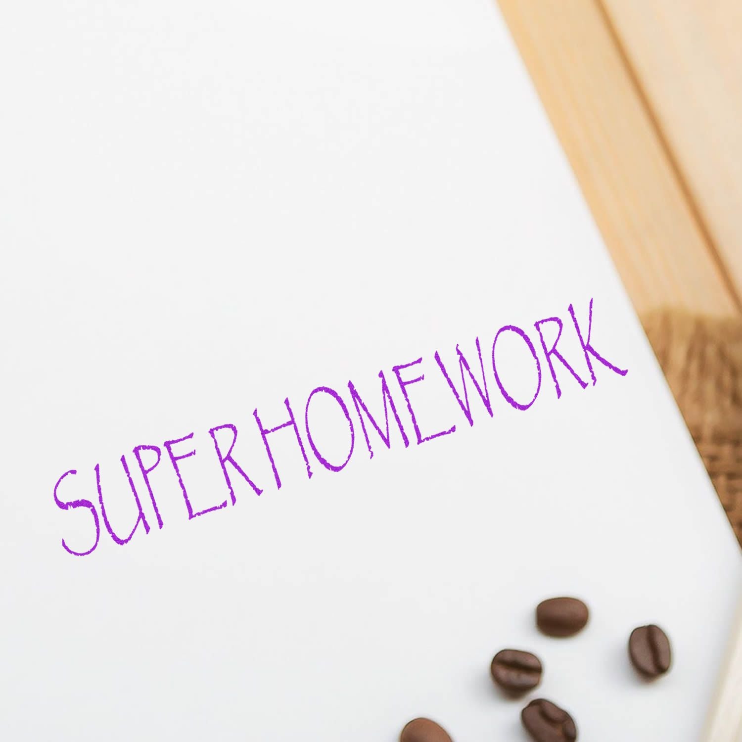 Super Homework Rubber Stamp in purple ink on white paper with coffee beans nearby on a wooden surface.