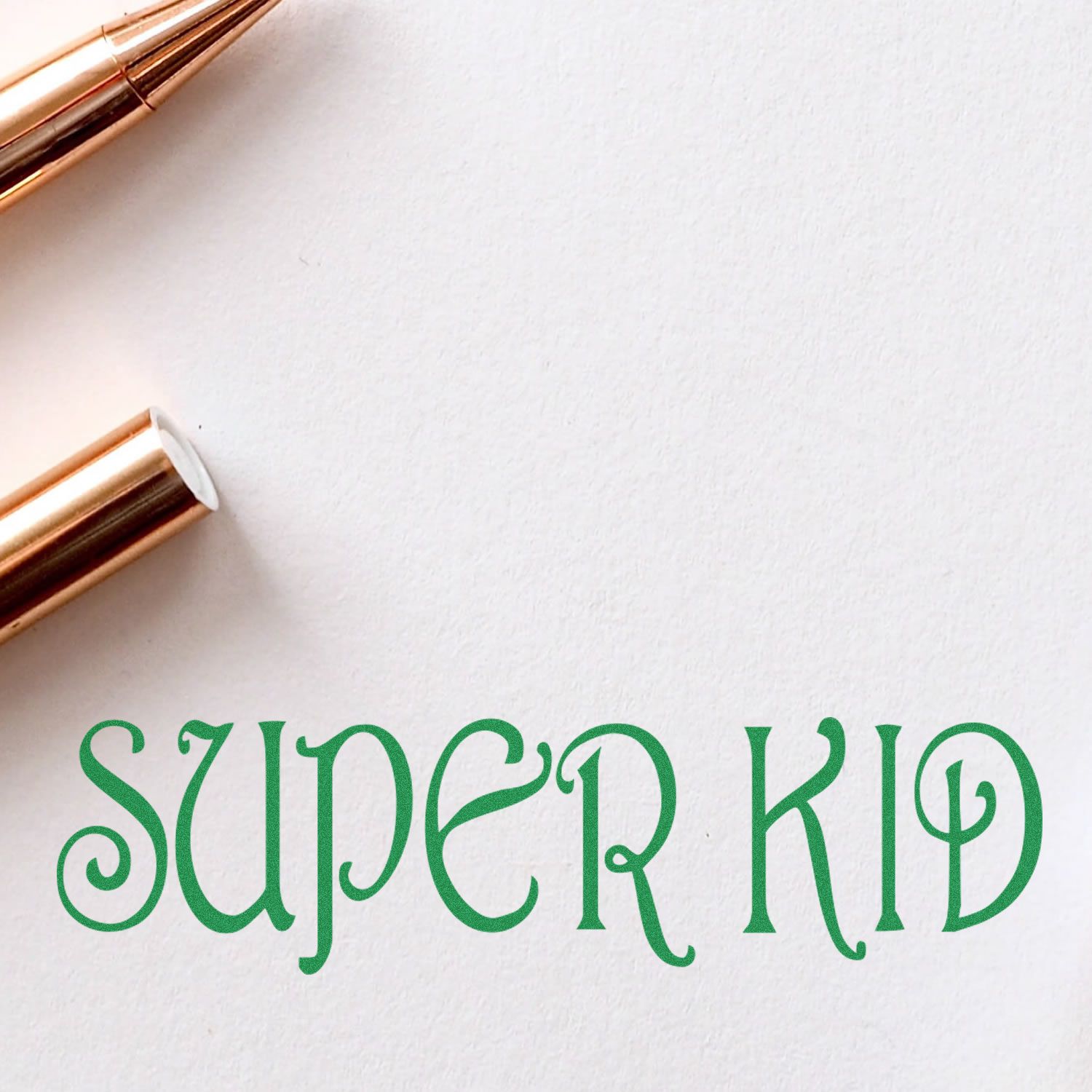 Self Inking Super Kid Stamp in use, showing the green SUPER KID imprint on white paper next to a gold pen.