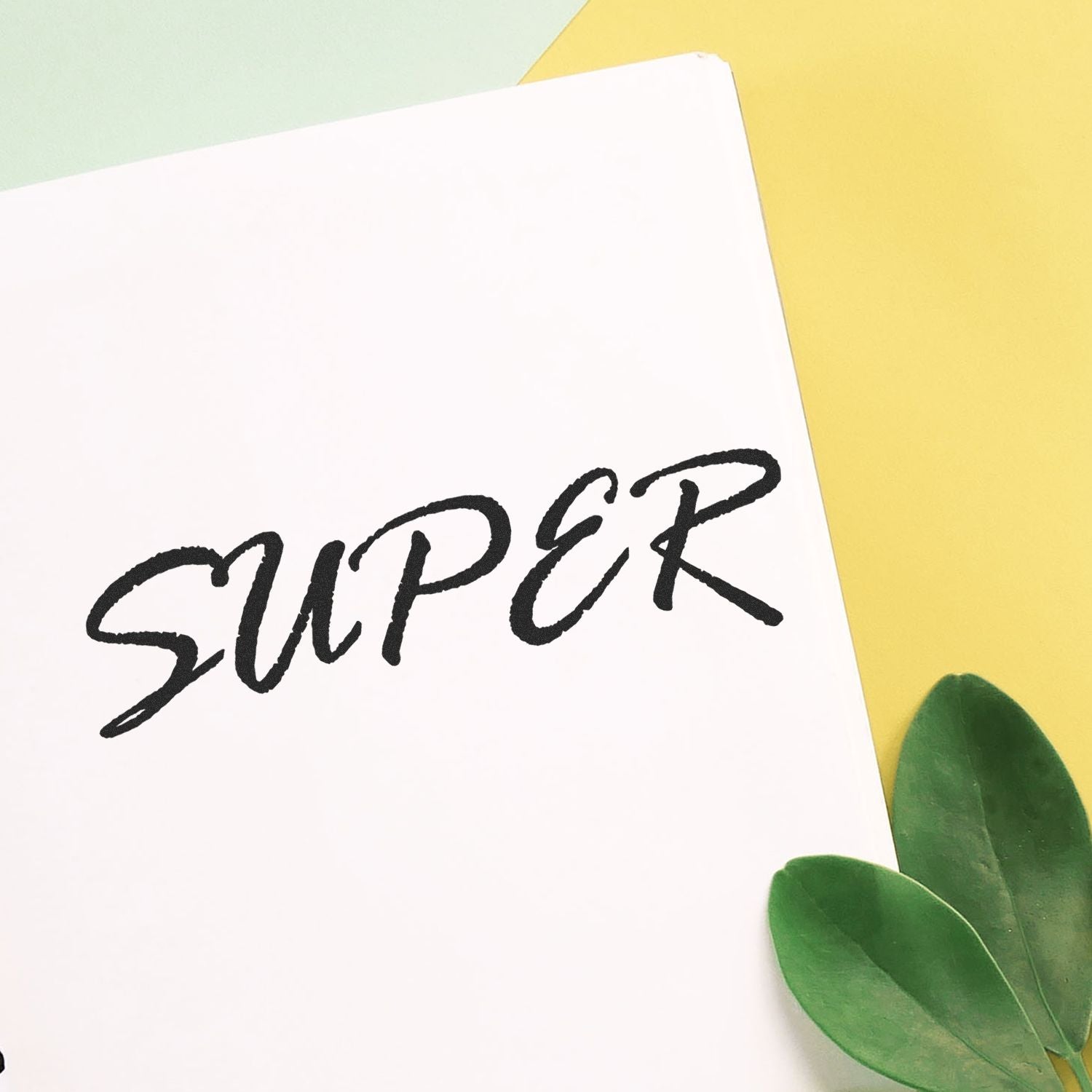 Large Pre-Inked Super Stamp imprinting the word 'SUPER' in bold black letters on white paper, with green leaves and yellow background.