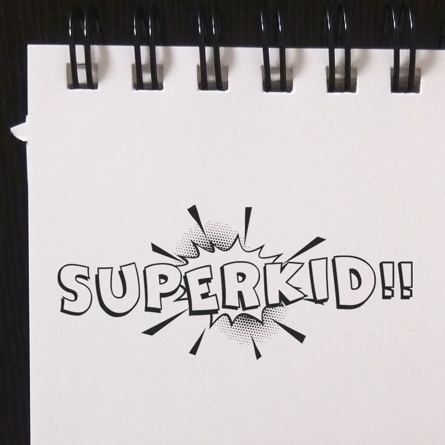 Self Inking Superkid Stamp imprint on a white notepad with black spiral binding, featuring bold comic-style SUPERKID!! text.