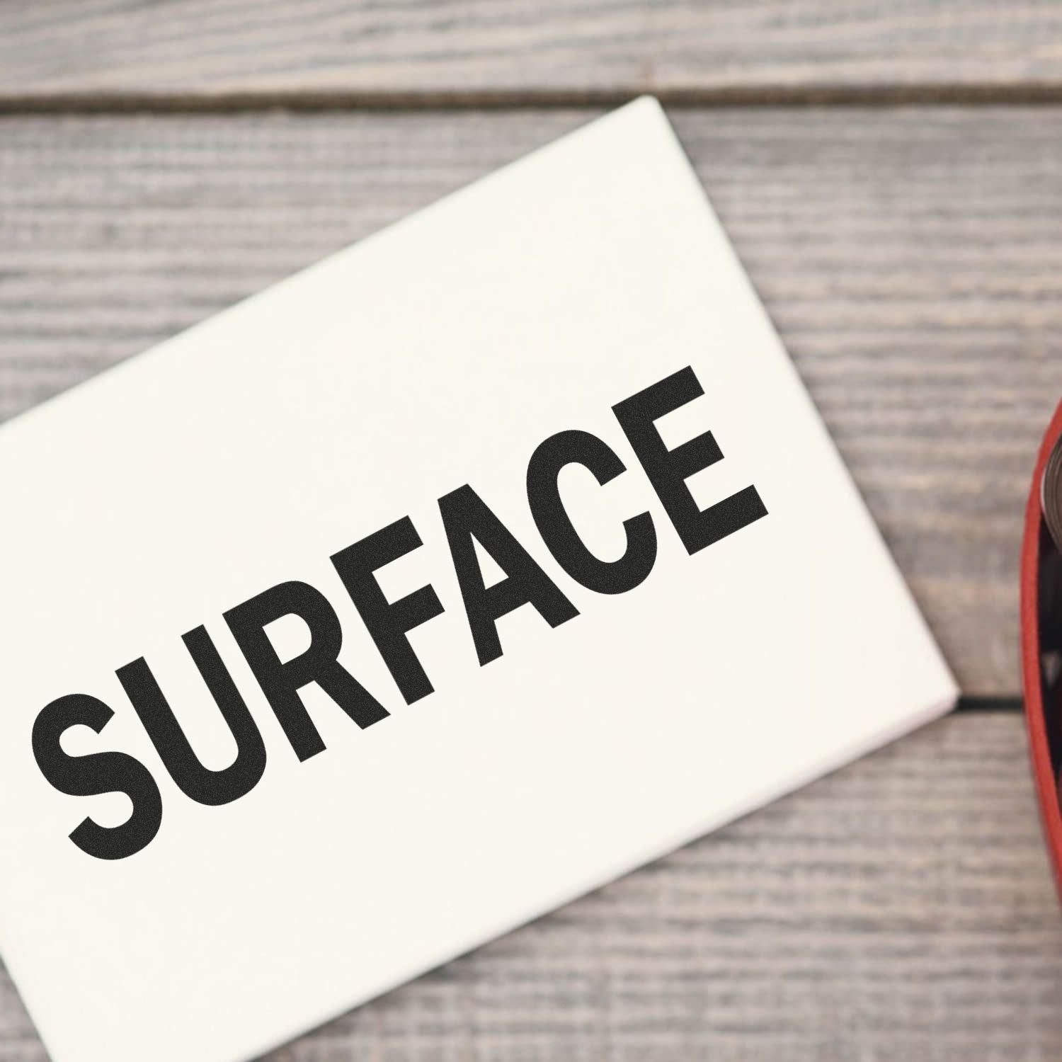 A Slim Pre-Inked Surface Stamp marking the word SURFACE on a white card, placed on a wooden table.