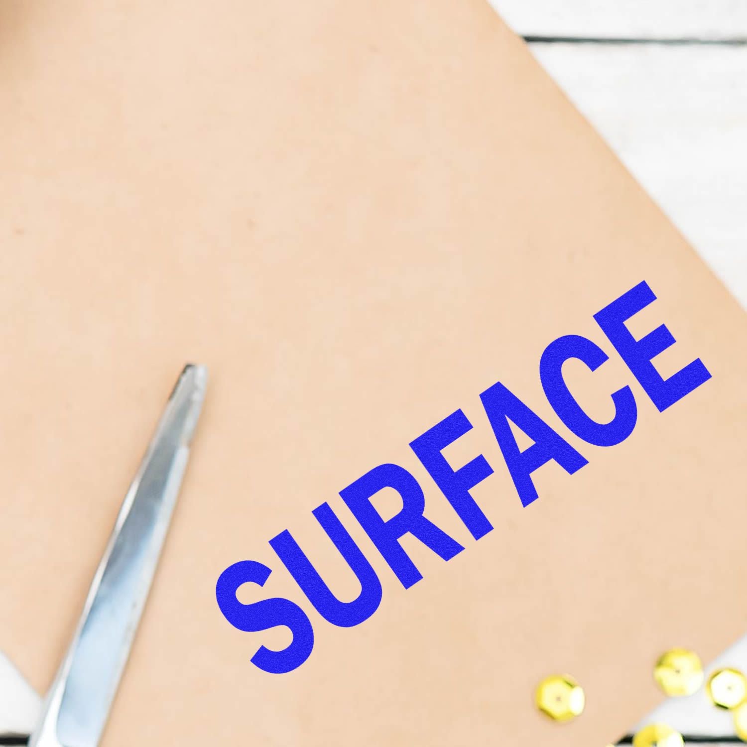 Surface rubber stamp in blue ink on a beige sheet with a pair of scissors and yellow sequins nearby.