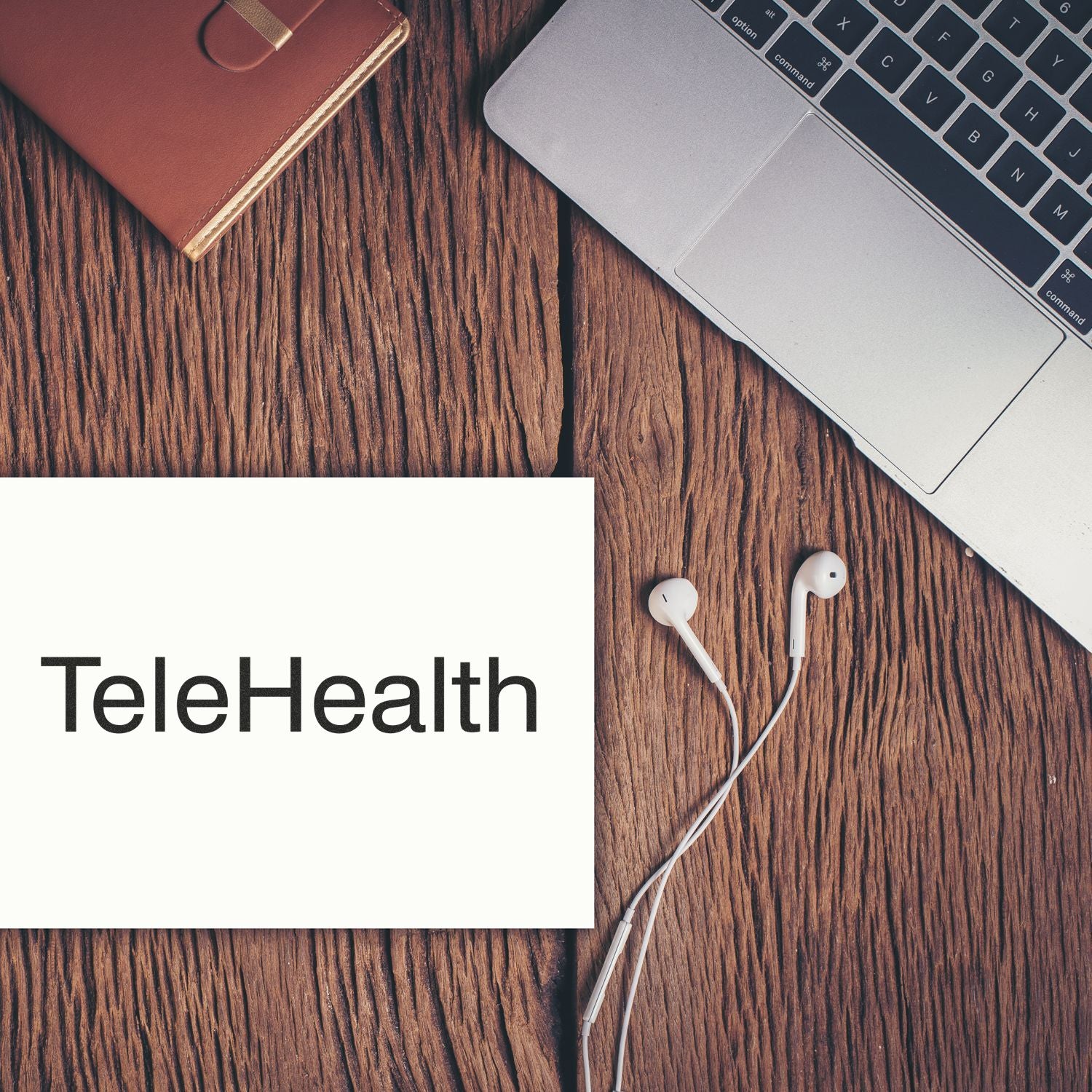 TeleHealth rubber stamp on a wooden desk next to a laptop, earphones, and a brown notebook.