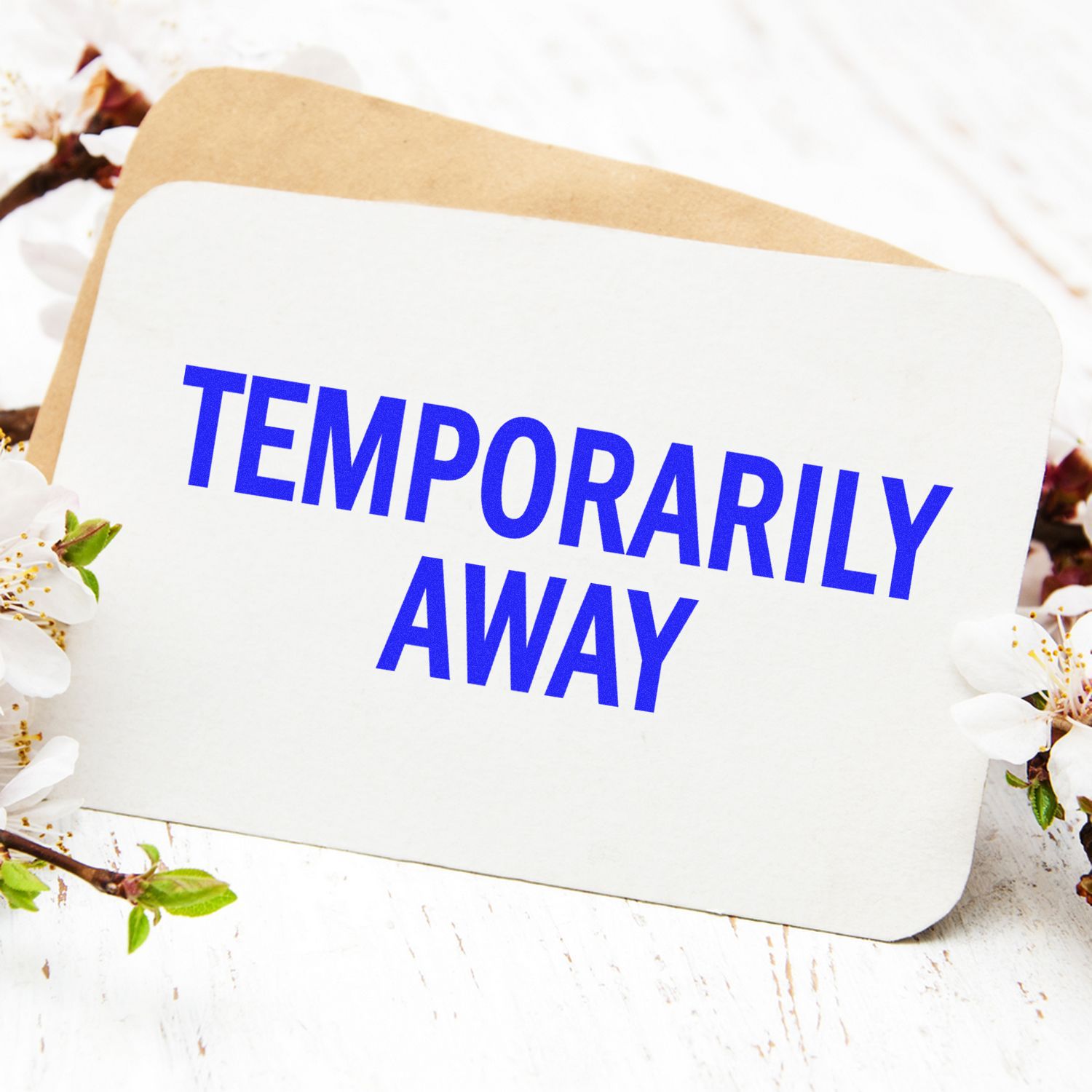 Temporarily Away Rubber Stamp on a white card with blue text, surrounded by white flowers and a brown envelope in the background.