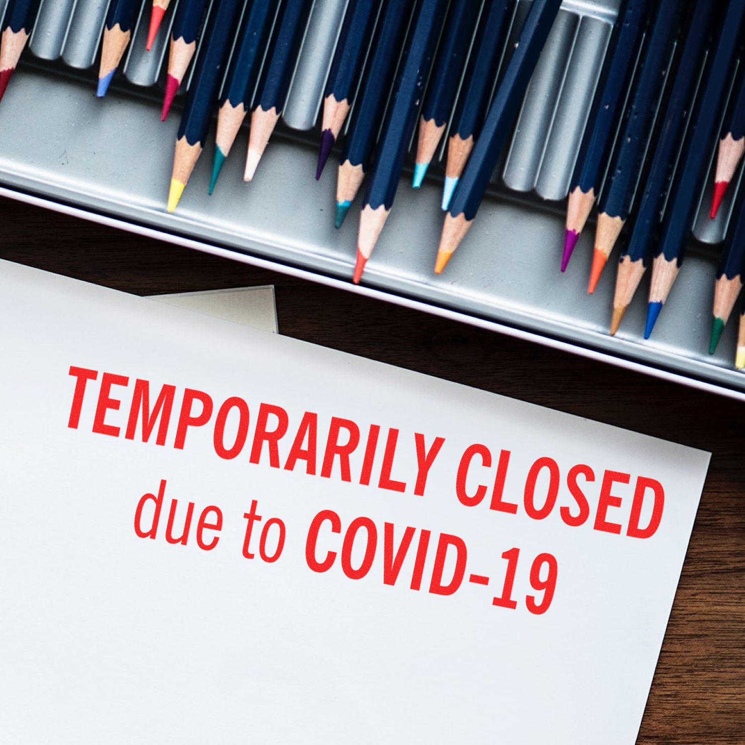 Large temporarily closed rubber stamp on paper with colored pencils in the background, indicating closure due to COVID-19.