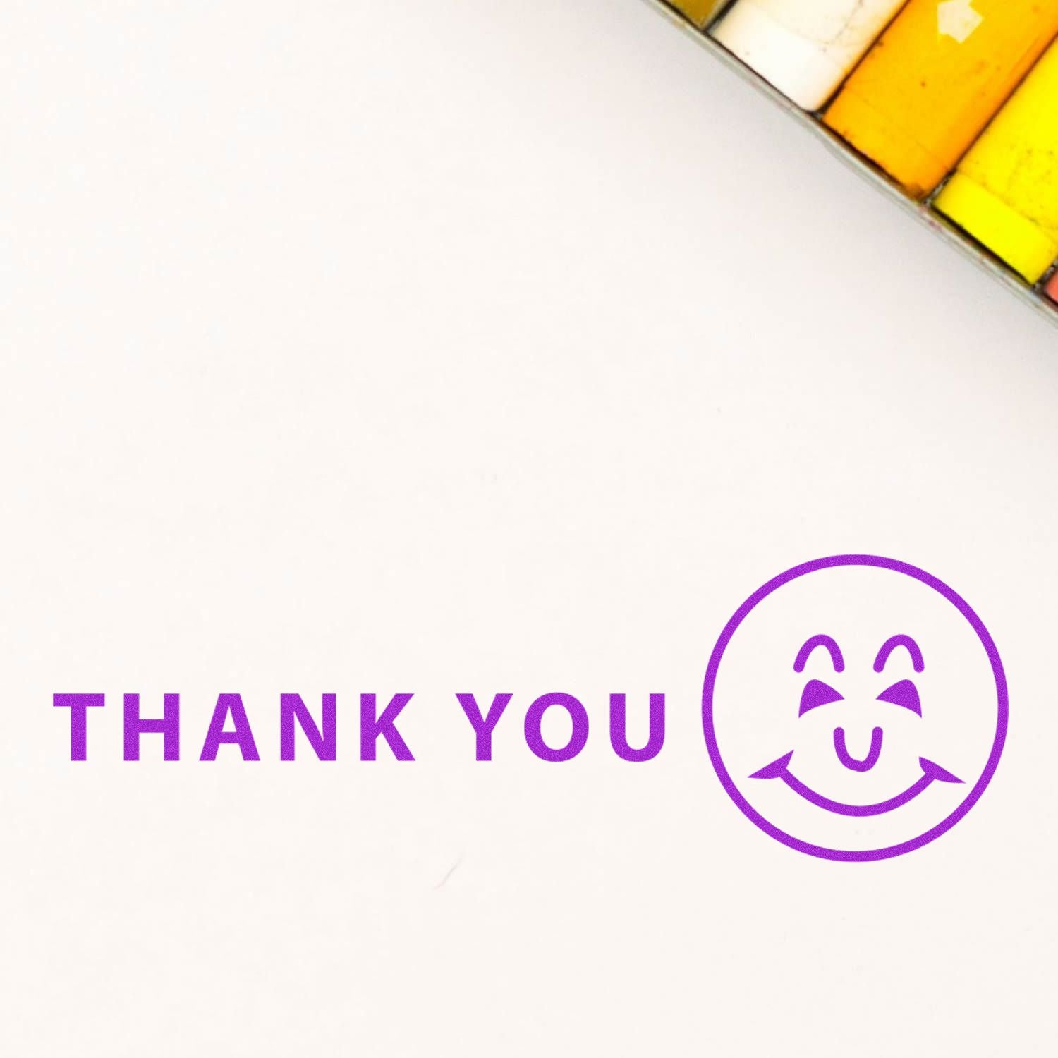 Large Thank You with Smiley Rubber Stamp in purple ink on white paper, with colored pencils in the background.