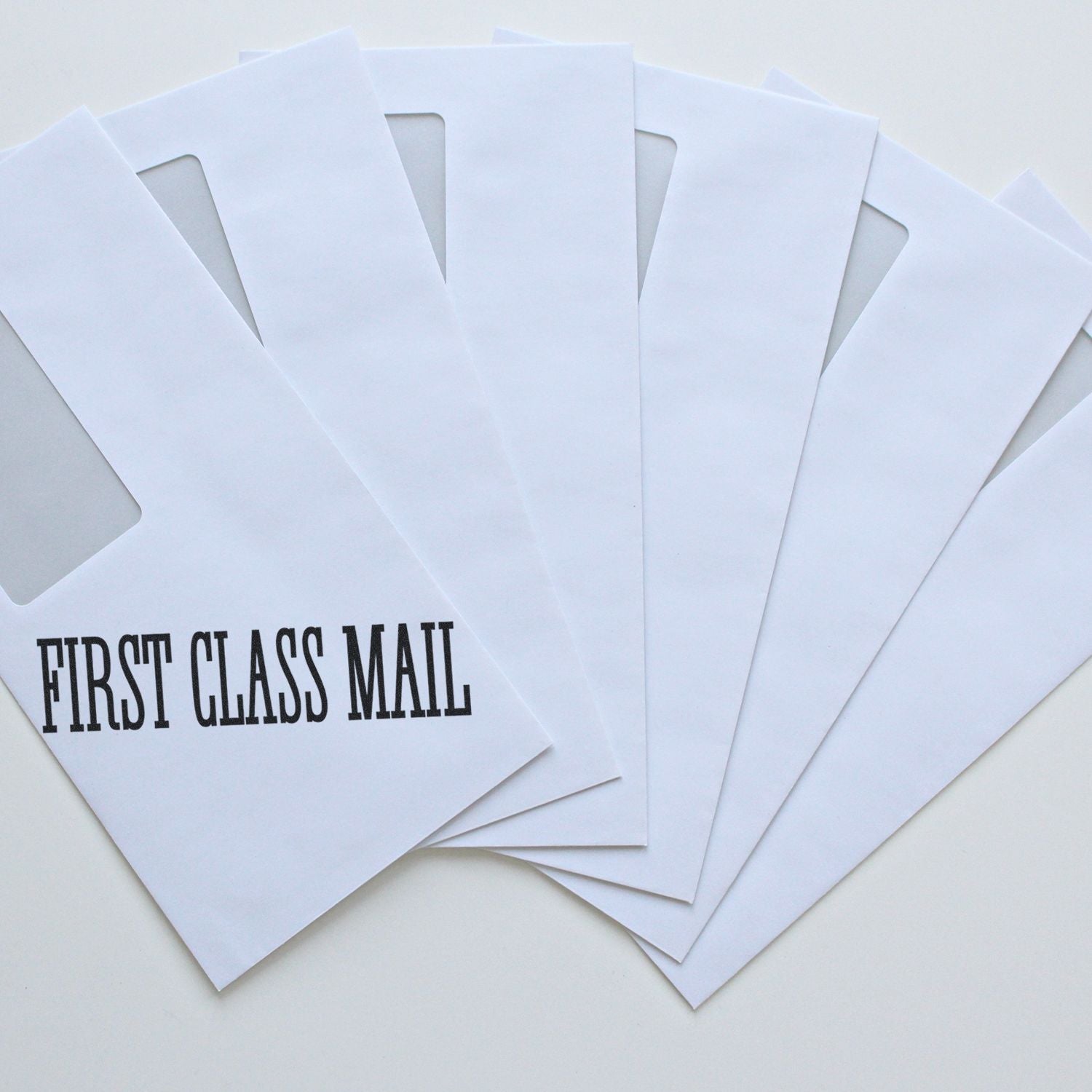 White envelopes stamped with FIRST CLASS MAIL using a Times First Class Mail Rubber Stamp, fanned out on a white surface.