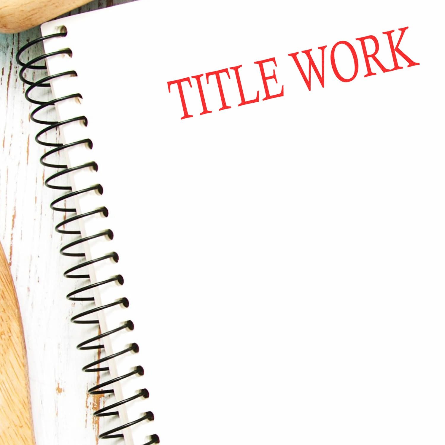 A spiral notebook with TITLE WORK stamped in red ink on a white page, placed on a wooden surface.