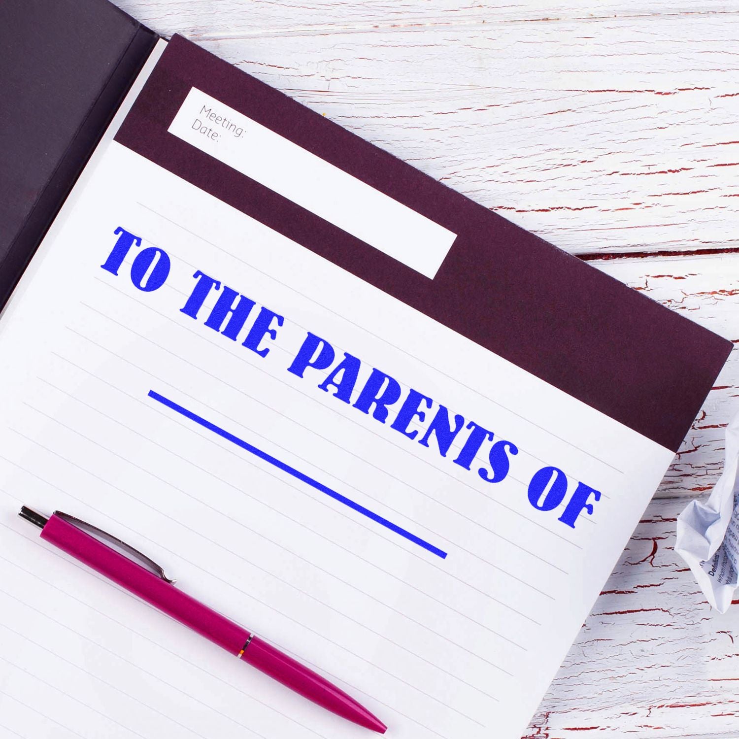 Notebook with TO THE PARENTS OF stamped in blue using the Self Inking To The Parents Of Stamp, alongside a pink pen on a white wooden table.