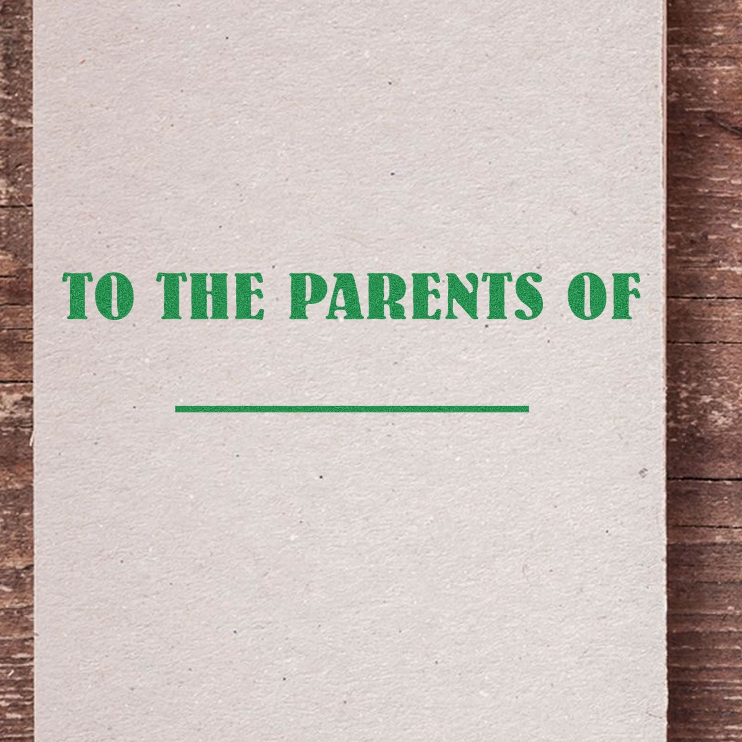 Slim Pre-Inked To The Parents Of Stamp in green text on a beige card with a wooden background.