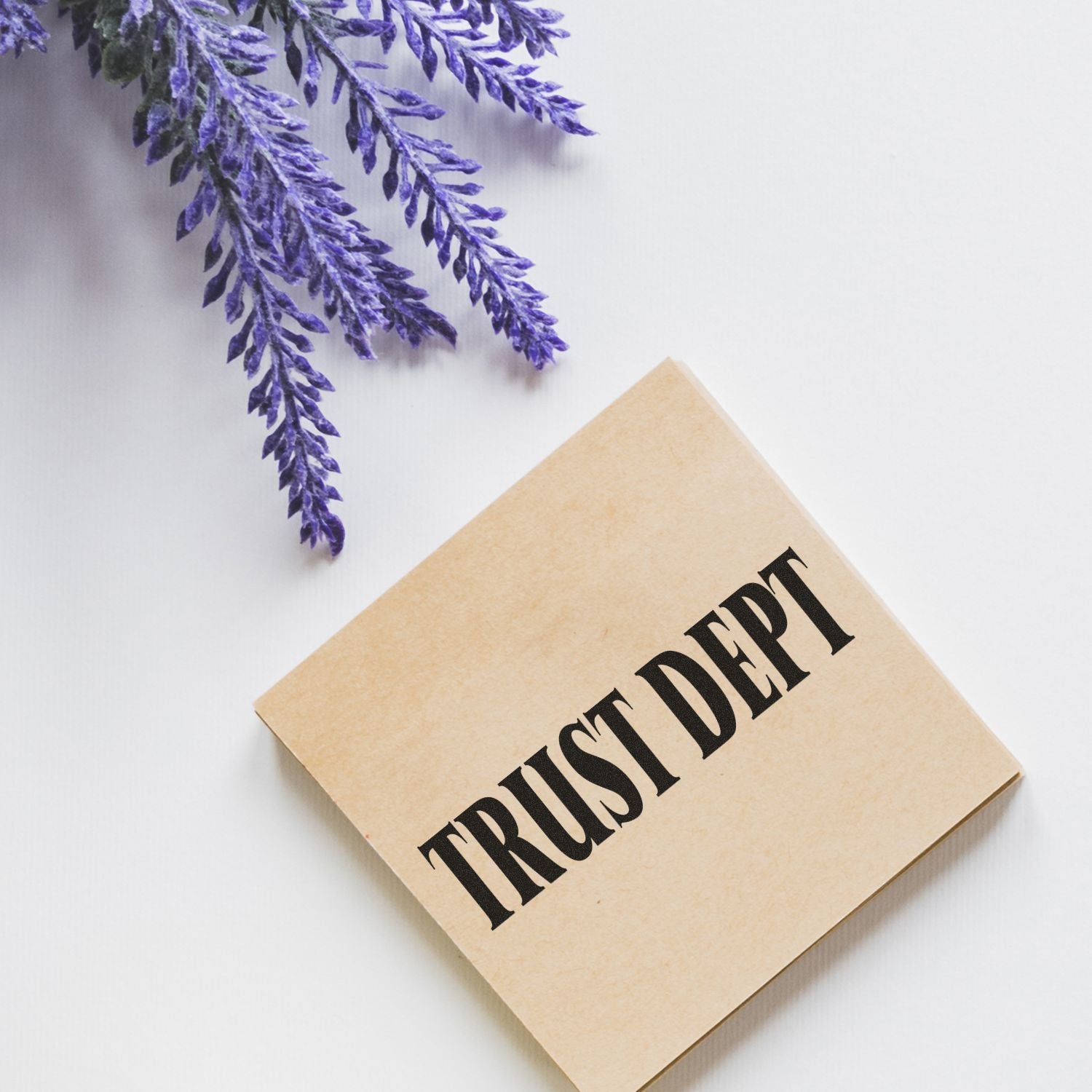 Trust Dept rubber stamp on a beige square block, placed on a white surface next to purple lavender flowers.