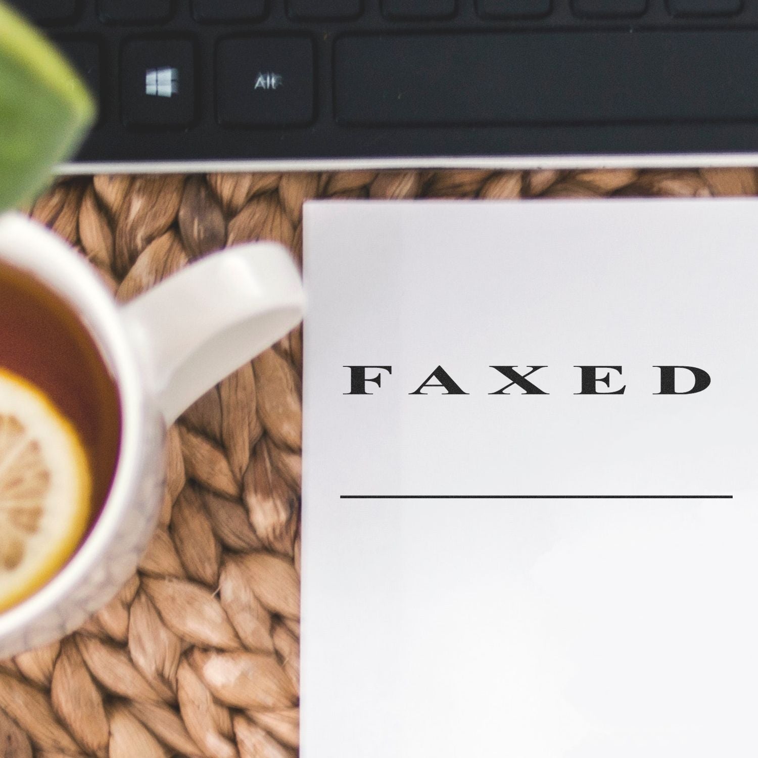 Self Inking Two Line Faxed Stamp marking a document on a woven mat beside a cup of tea with lemon and a keyboard.