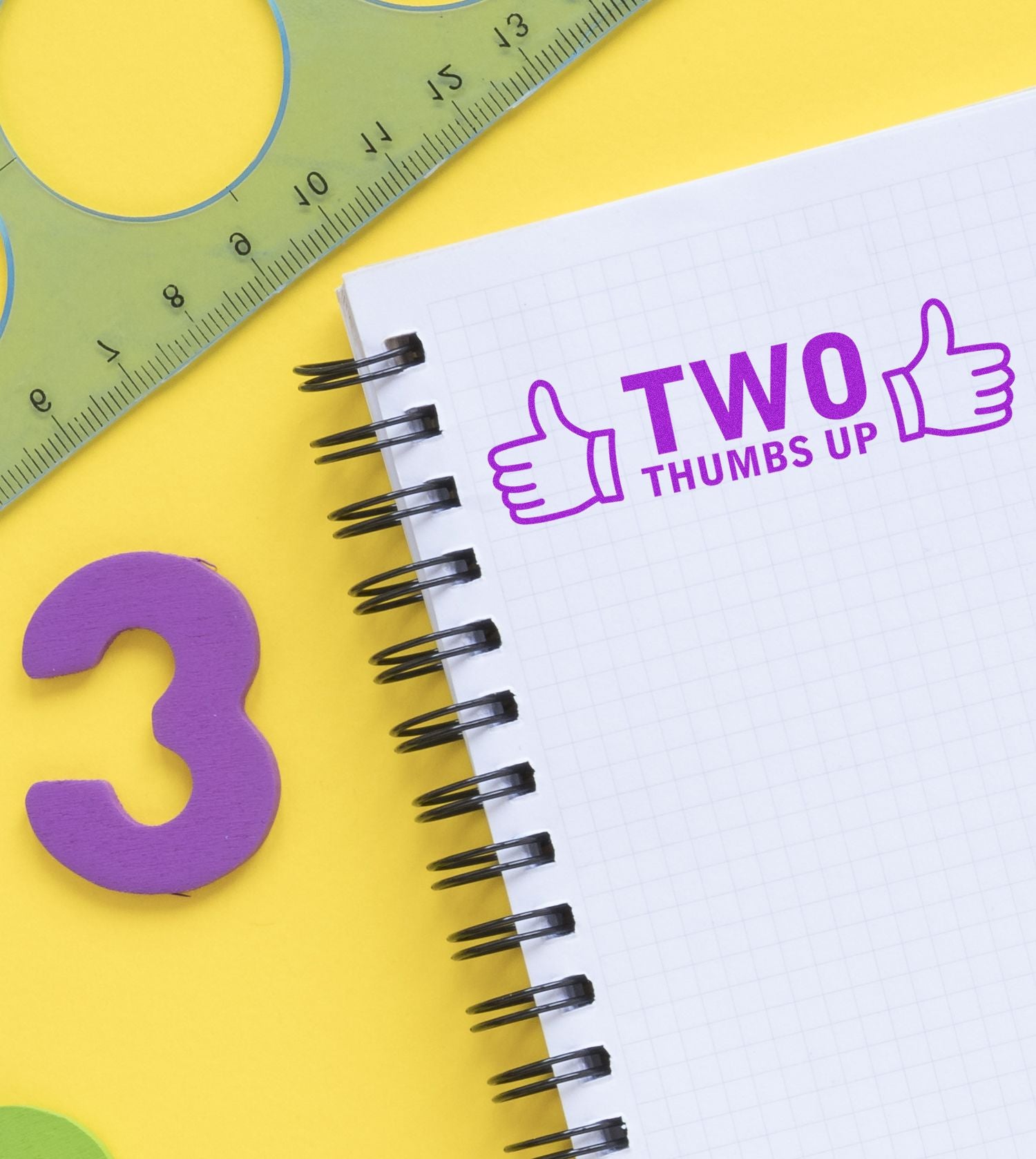 Notebook with 'Two Thumbs Up with Thumb Icon Rubber Stamp' in purple ink, surrounded by a ruler, number 3, and yellow background.