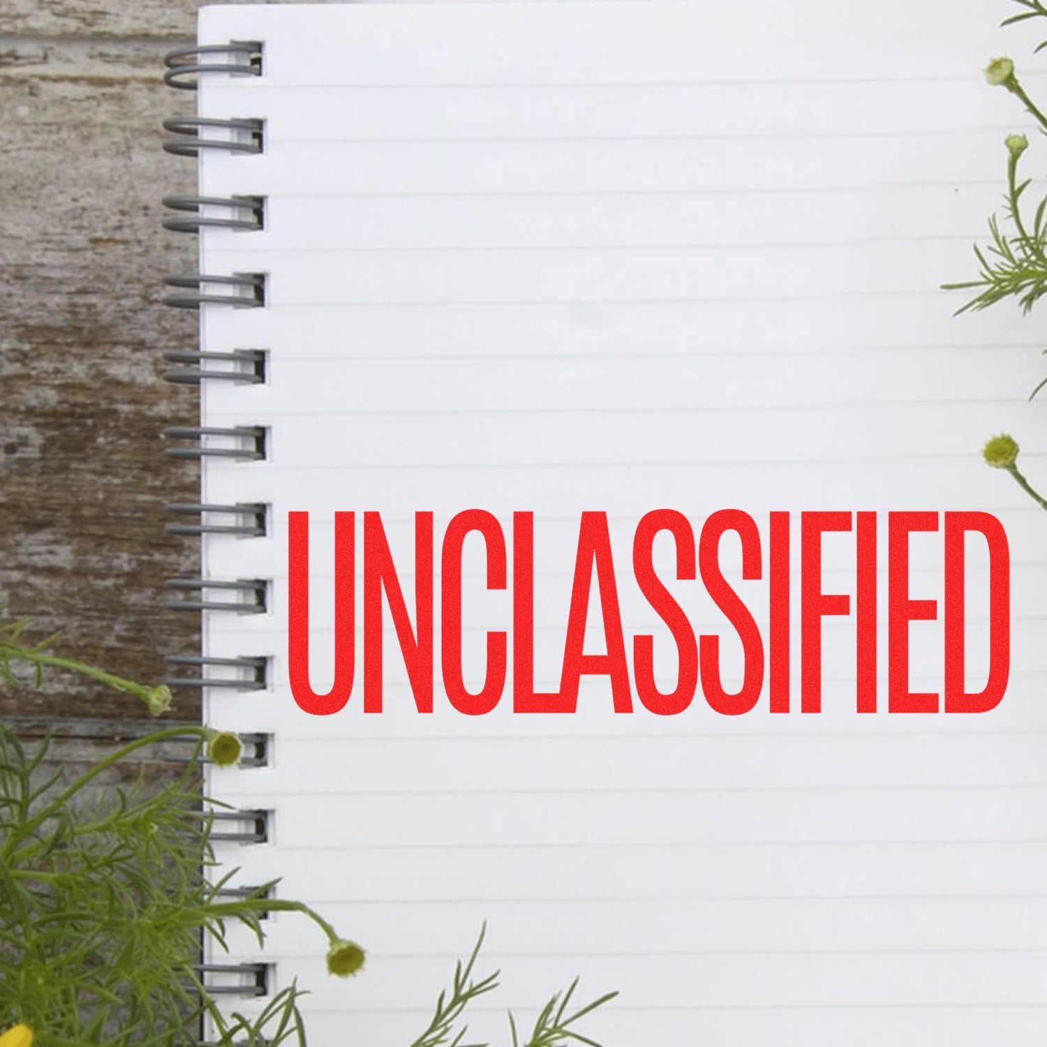 A notebook with a red UNCLASSIFIED mark stamped using a Self Inking Unclassified Stamp, surrounded by green plants.