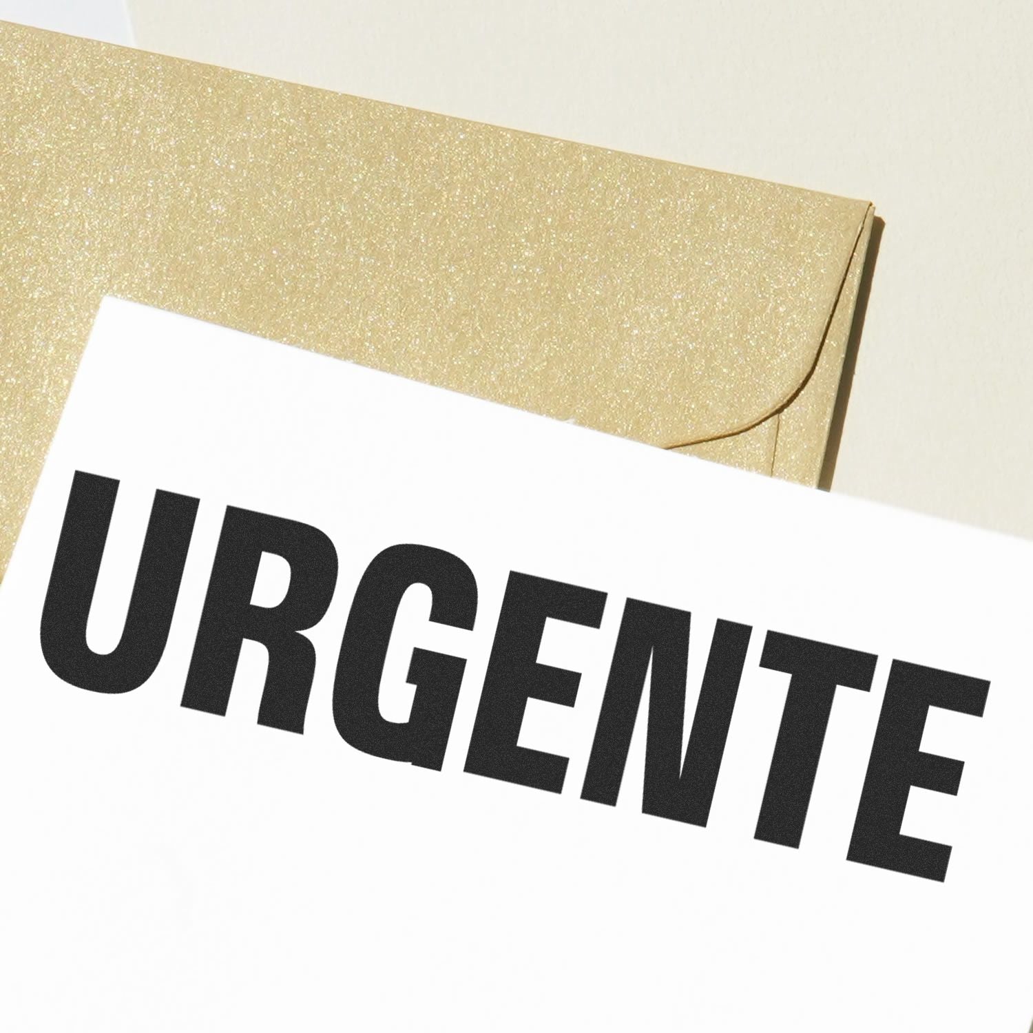 Urgente rubber stamp impression on white paper with a gold envelope in the background.