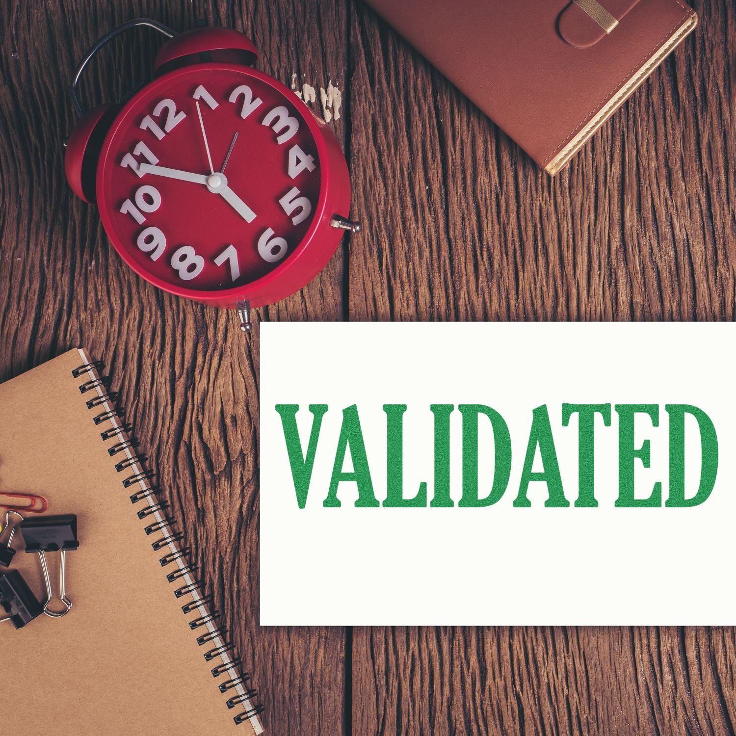 Desk with red clock, notebook, and paper stamped 'VALIDATED' using a Slim Pre-Inked Validated Stamp.