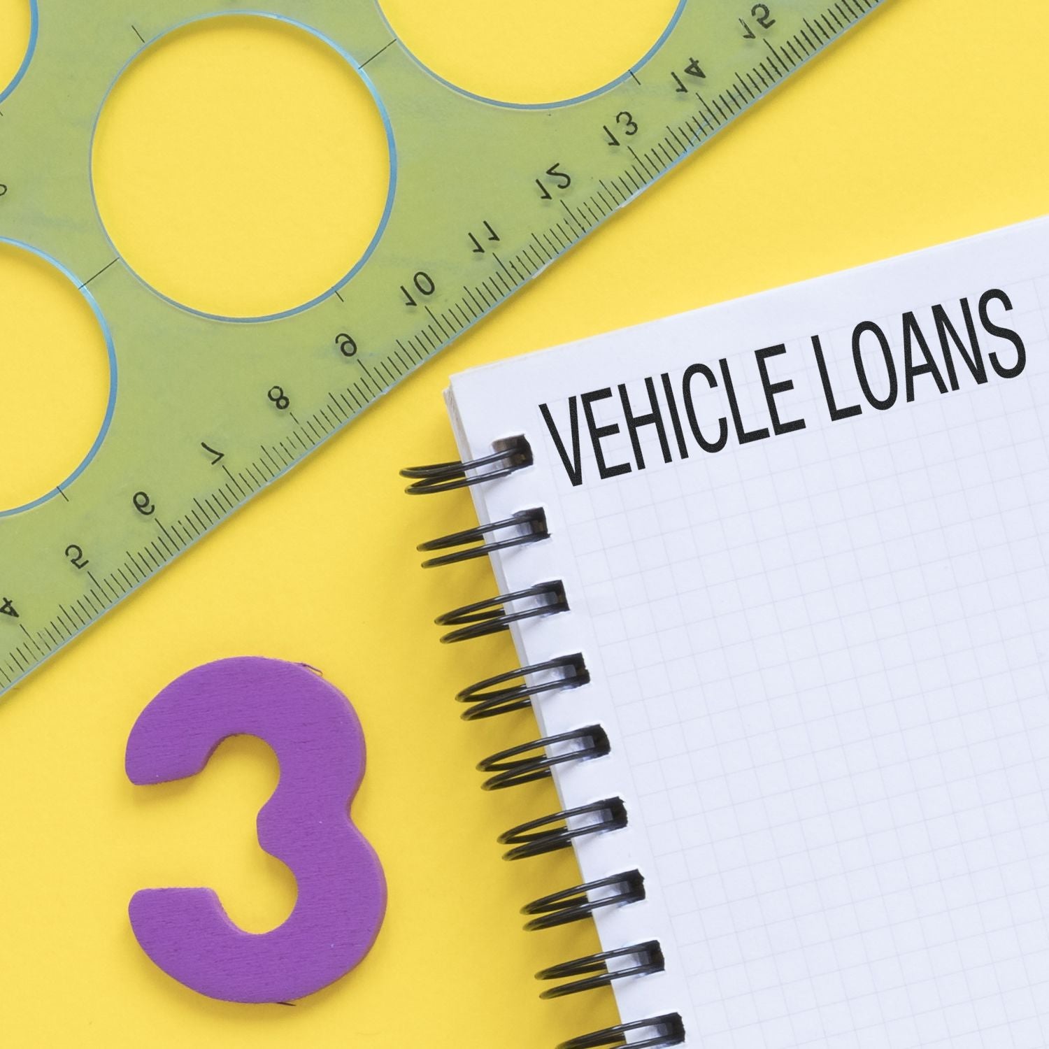 A notebook with Vehicle Loans written on it, a green ruler, and a purple number three on a yellow background.