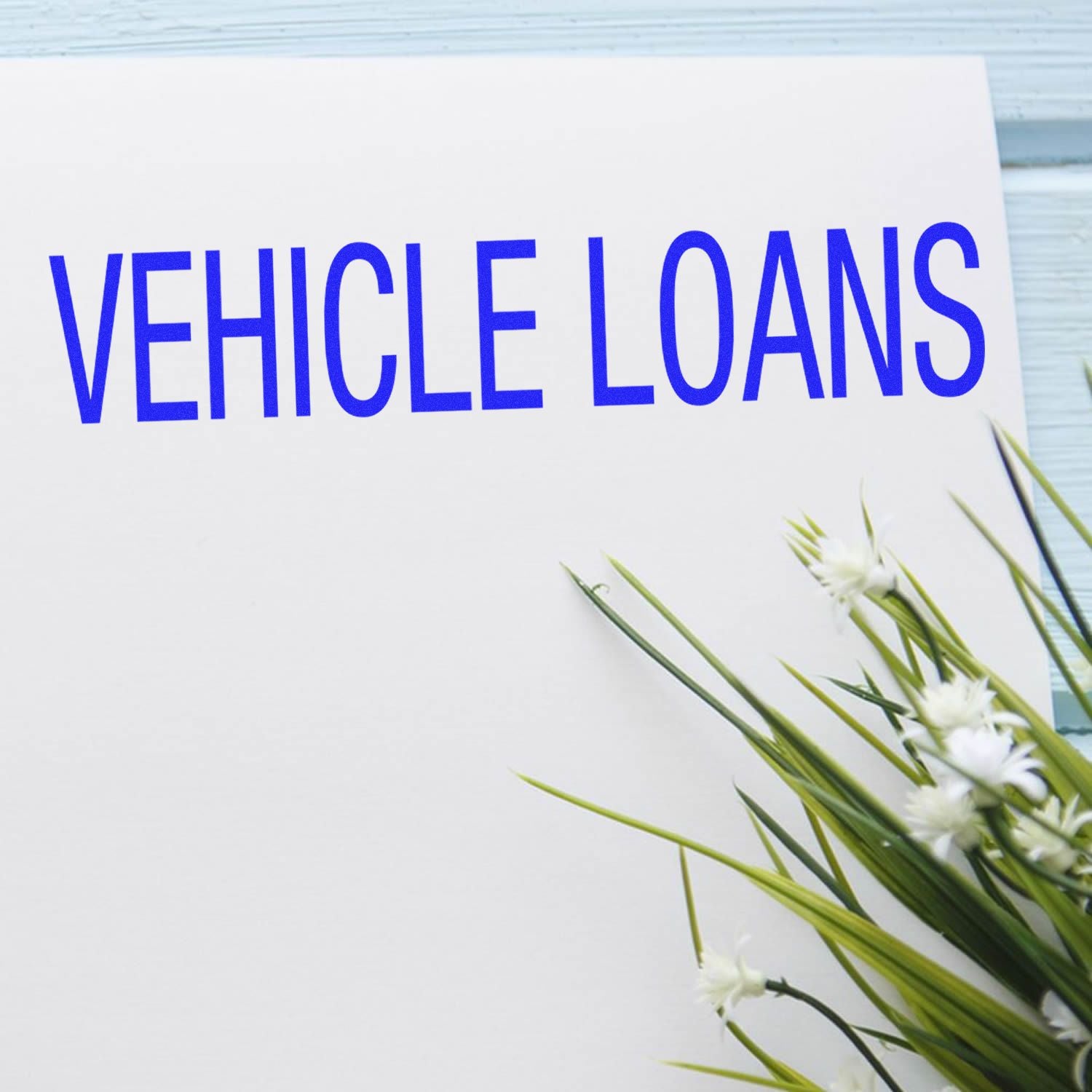 Slim Pre-Inked Vehicle Loans Stamp imprint on white paper with blue text, next to a small plant with white flowers.