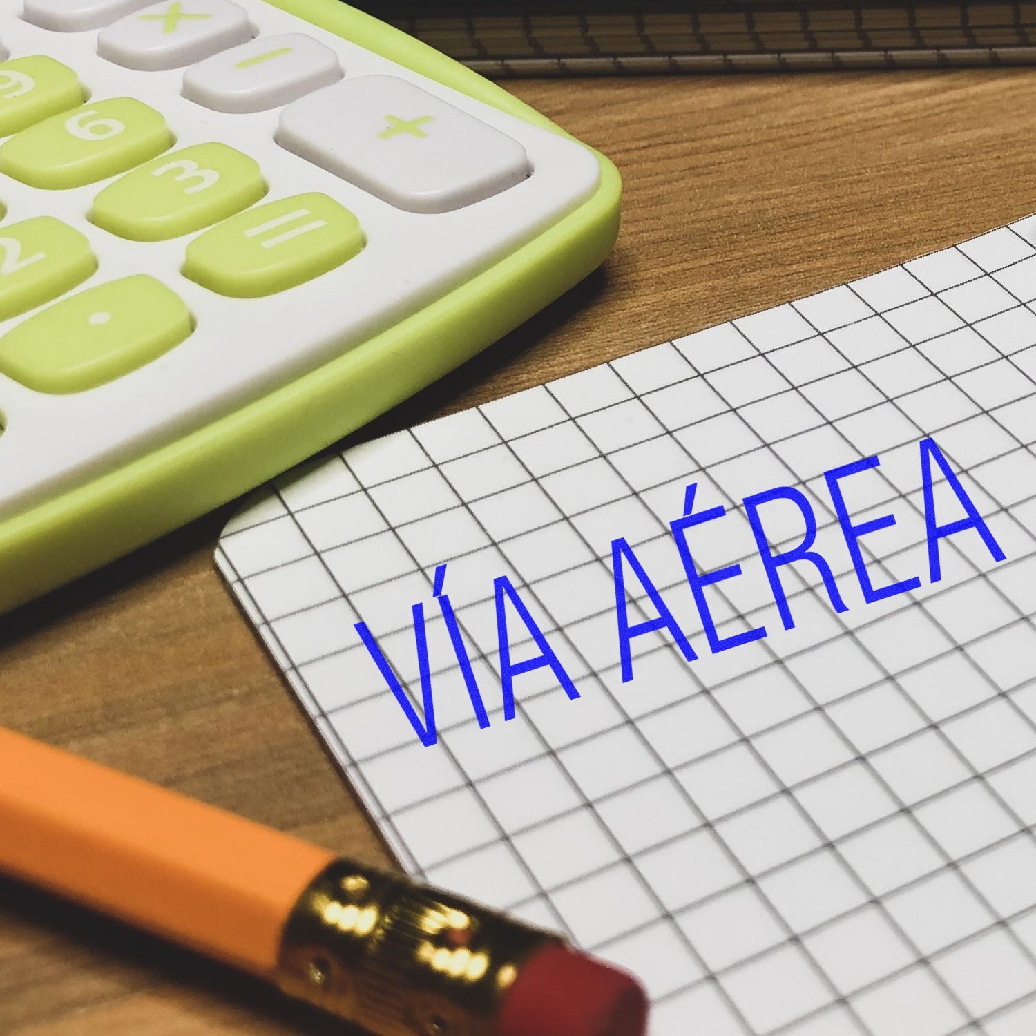 Self Inking Via Aerea Stamp used on graph paper, next to a pencil and a green calculator on a wooden desk.