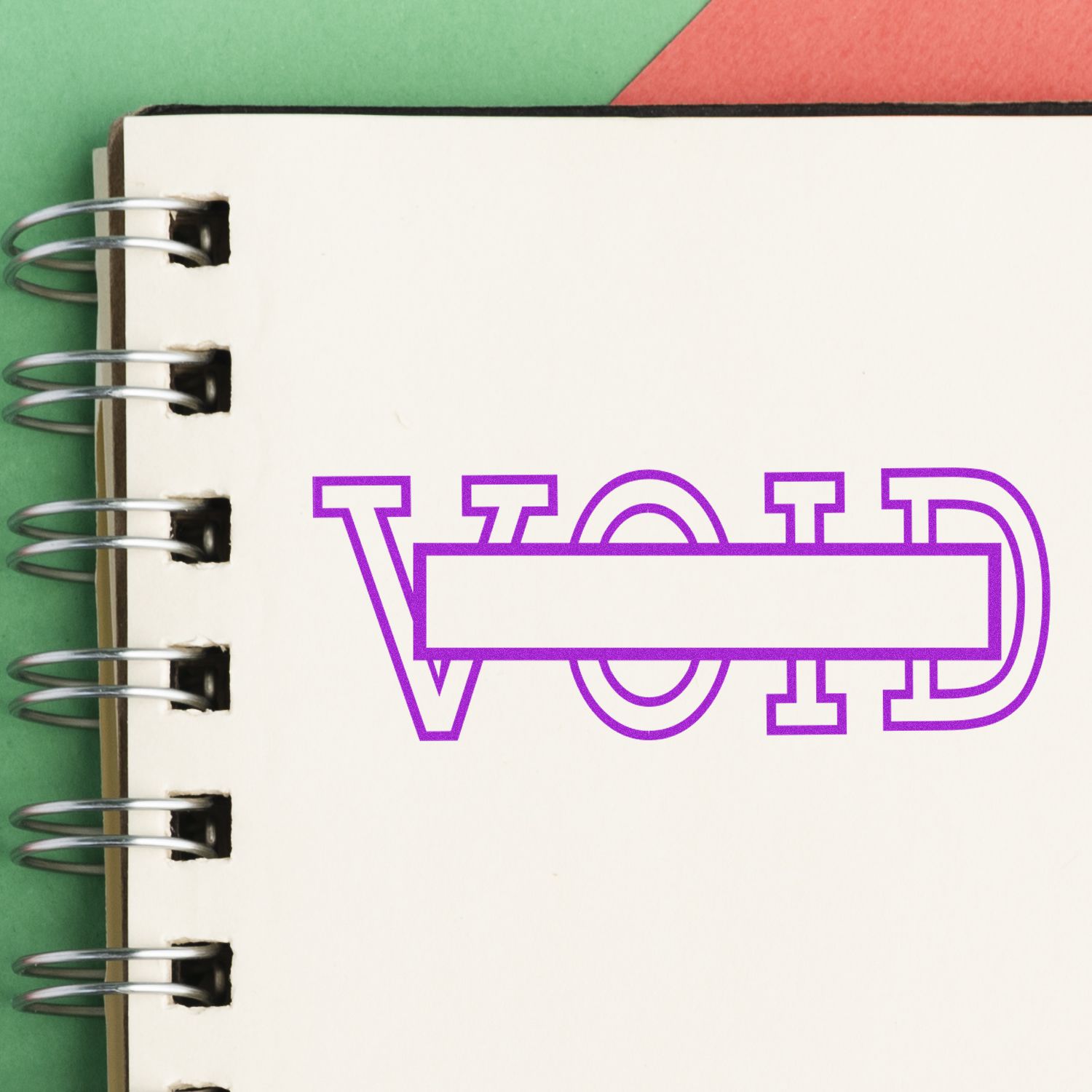 Large Self Inking Void with Box Stamp marking VOID in purple ink on a spiral notebook page with green and red background.