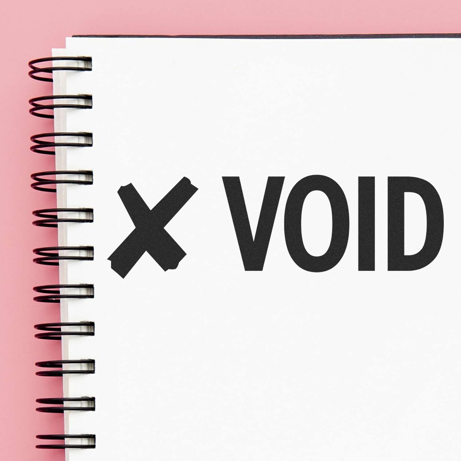 Notebook with a spiral binding showing a 'Void with X Rubber Stamp' mark on a white page against a pink background.