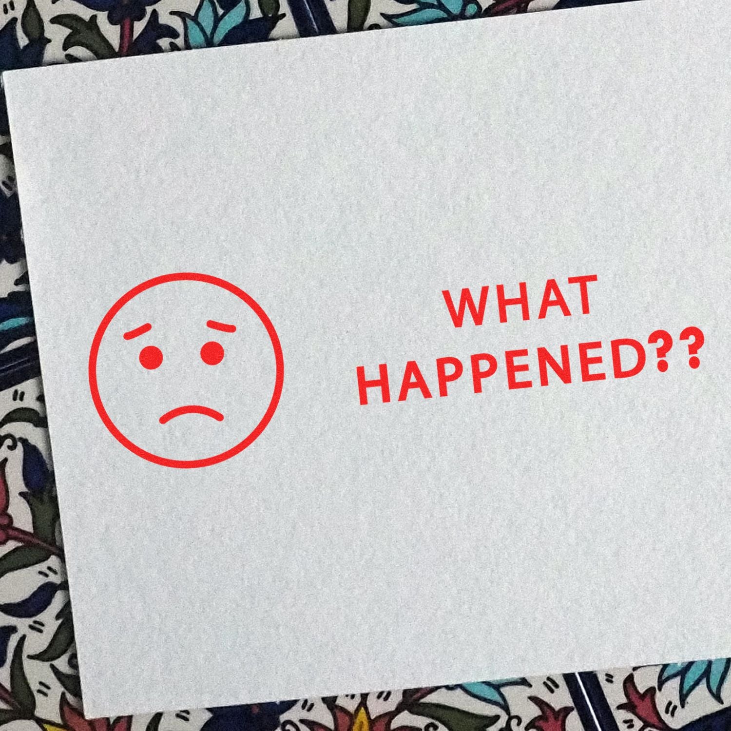 A white card with a red 'What Happened' rubber stamp and a sad face emoji on a colorful patterned background.