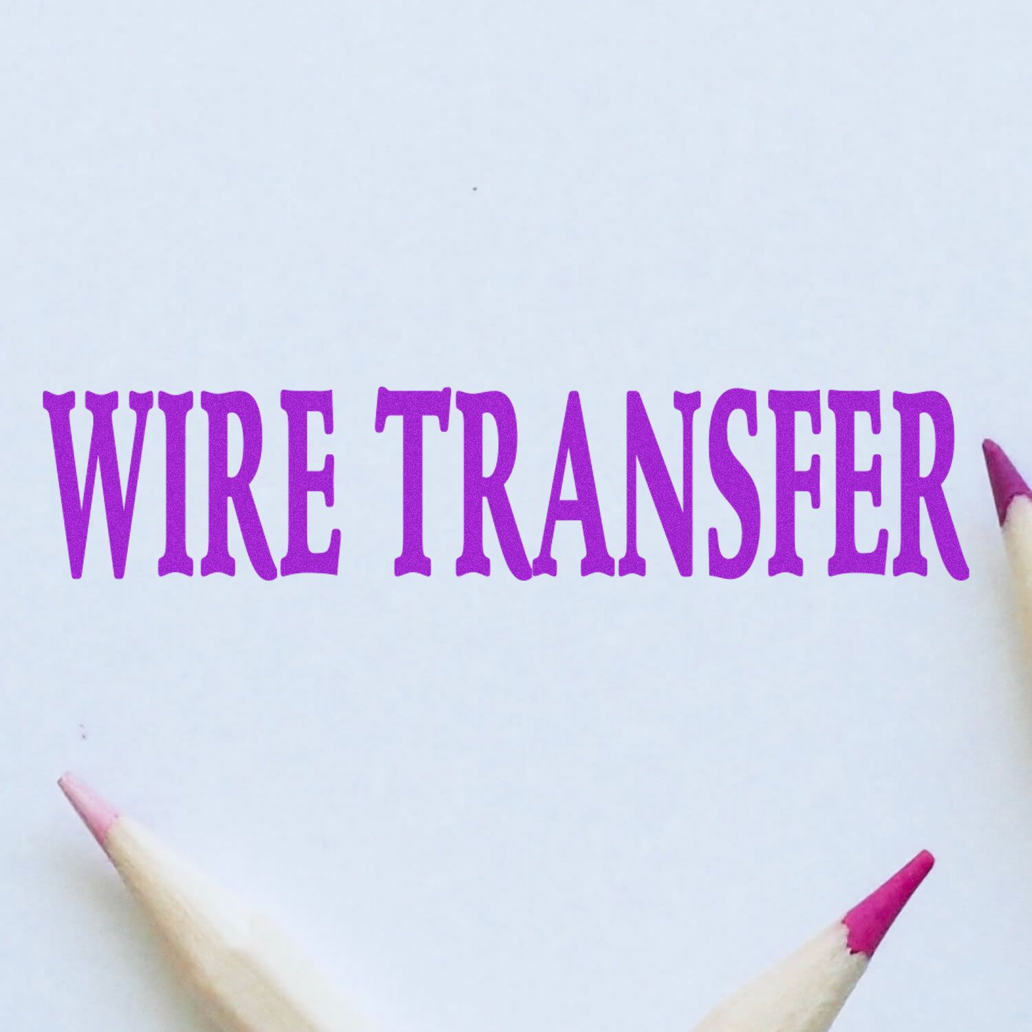 Wire Transfer Rubber Stamp in purple ink on white paper, surrounded by three colored pencils with pink tips.