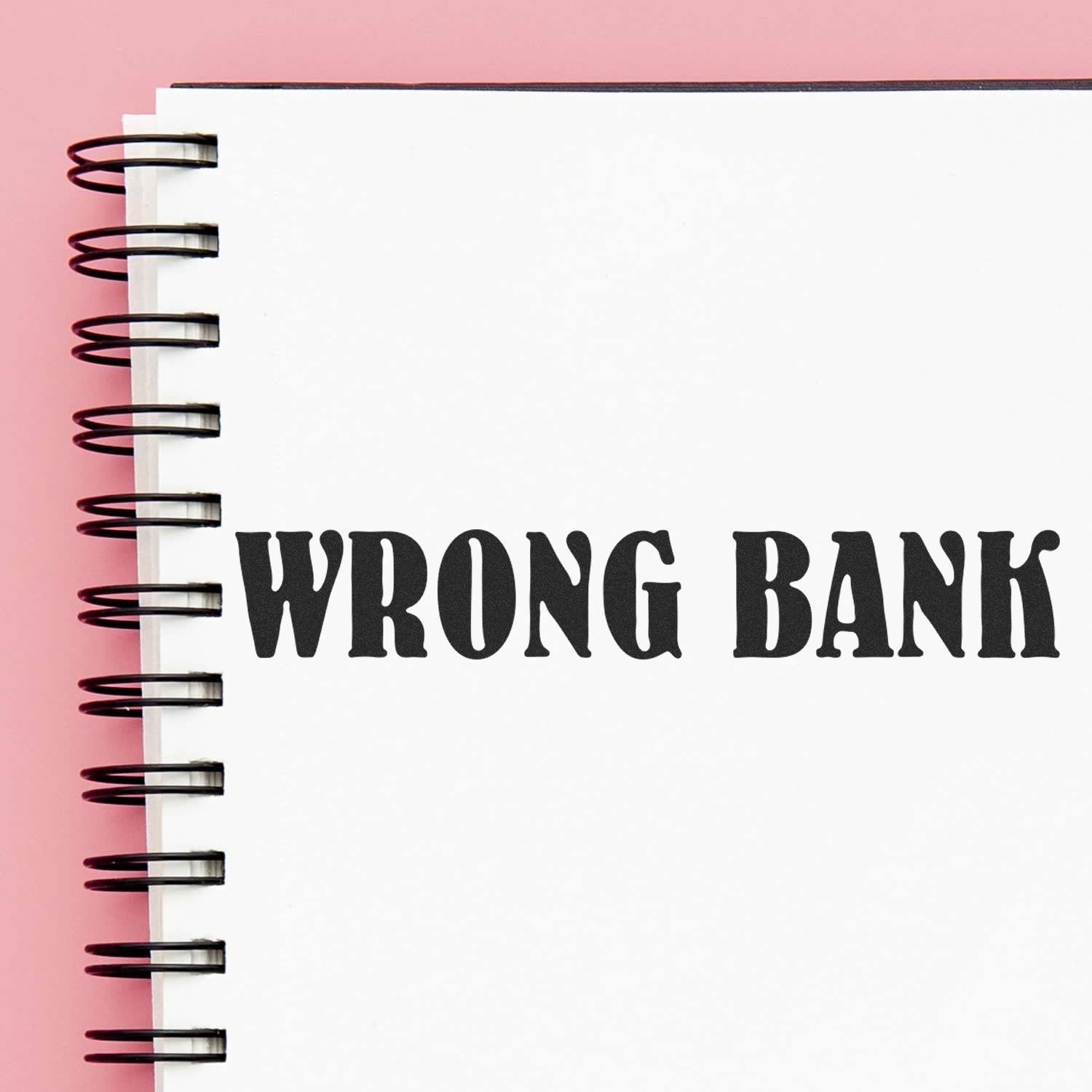 Self Inking Wrong Bank Stamp imprint on a white spiral notebook with a pink background.