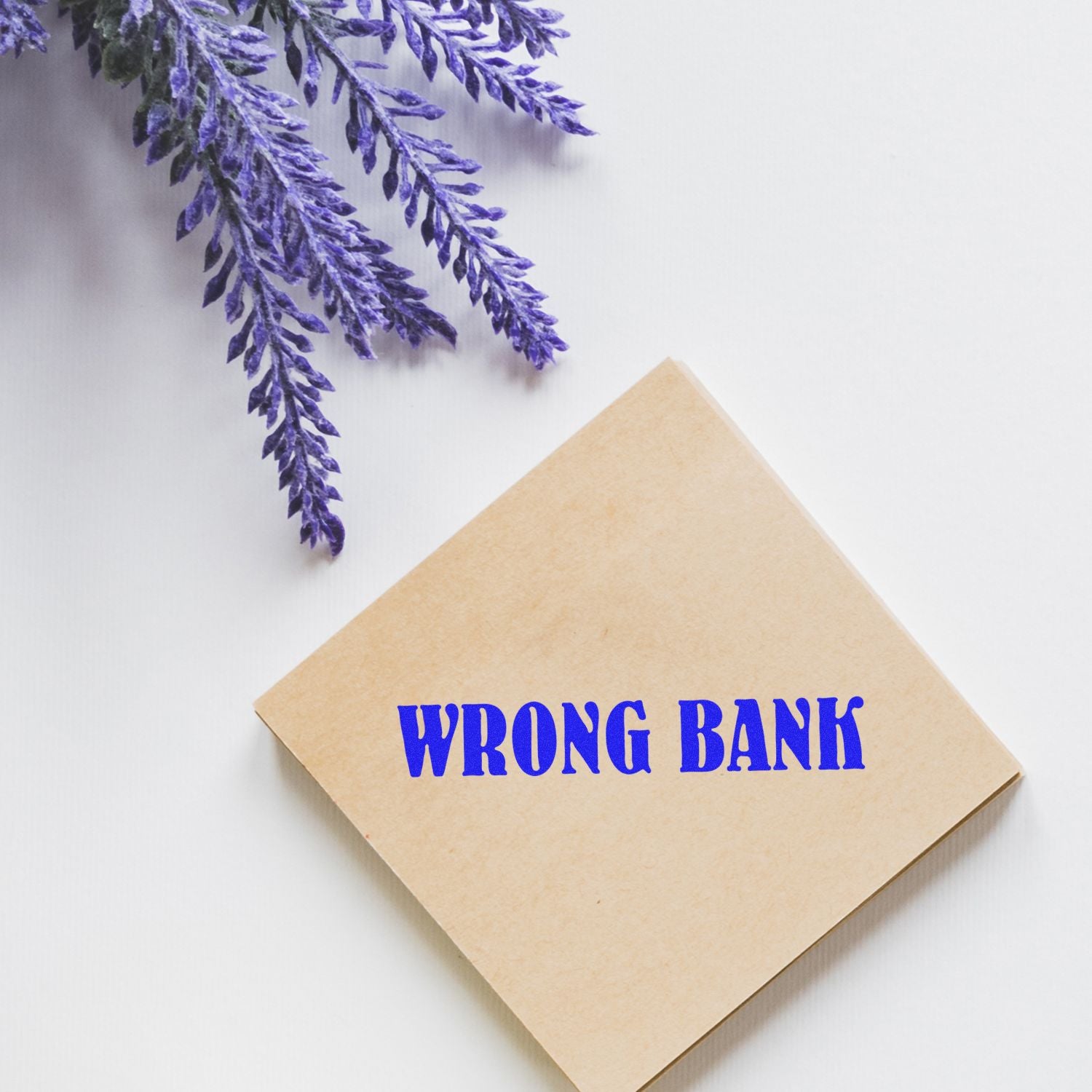 Self Inking Wrong Bank Stamp in blue ink on a brown envelope, placed next to lavender sprigs on a white background.