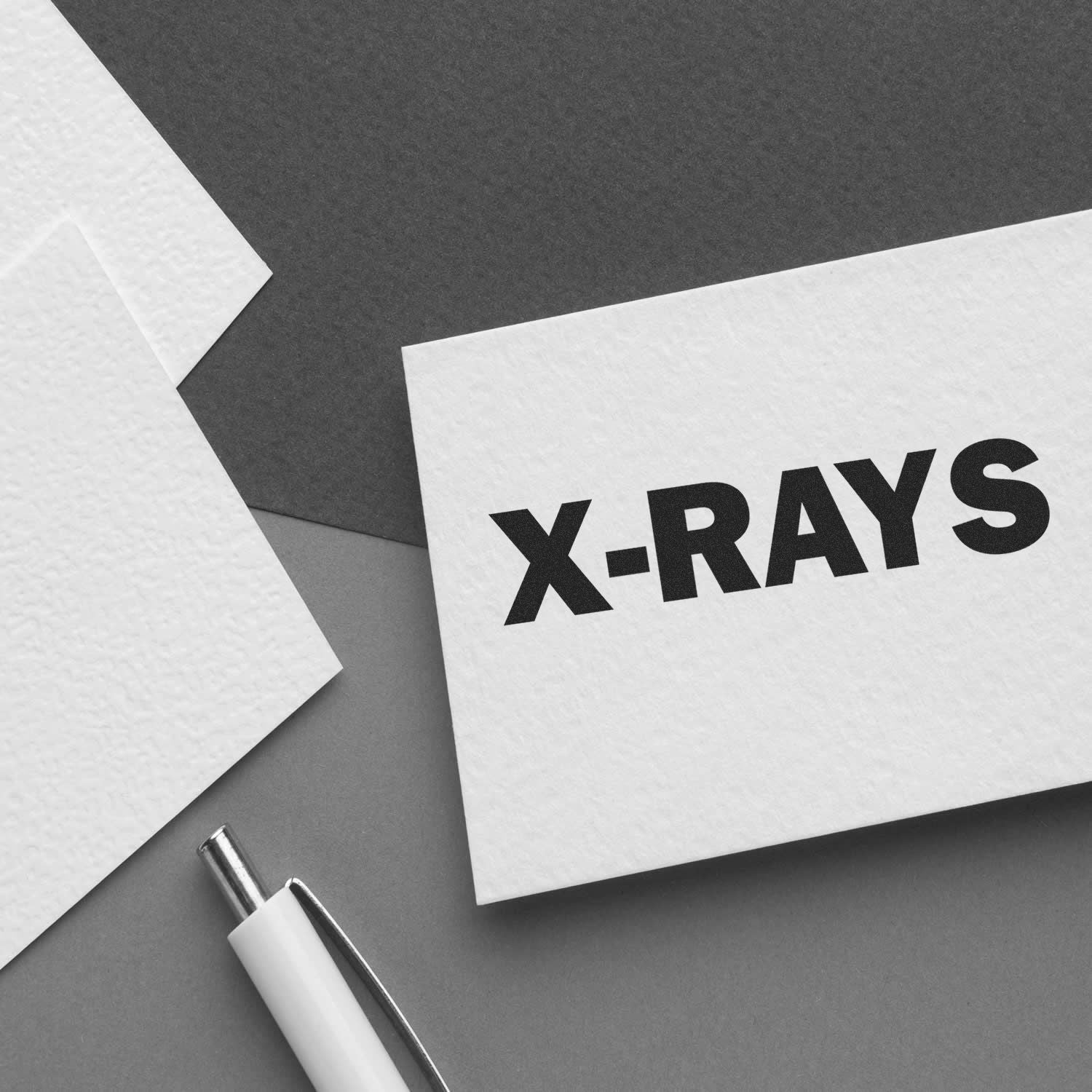 X-Rays Rubber Stamp used on white card, placed on a gray background with a pen and additional blank cards nearby.