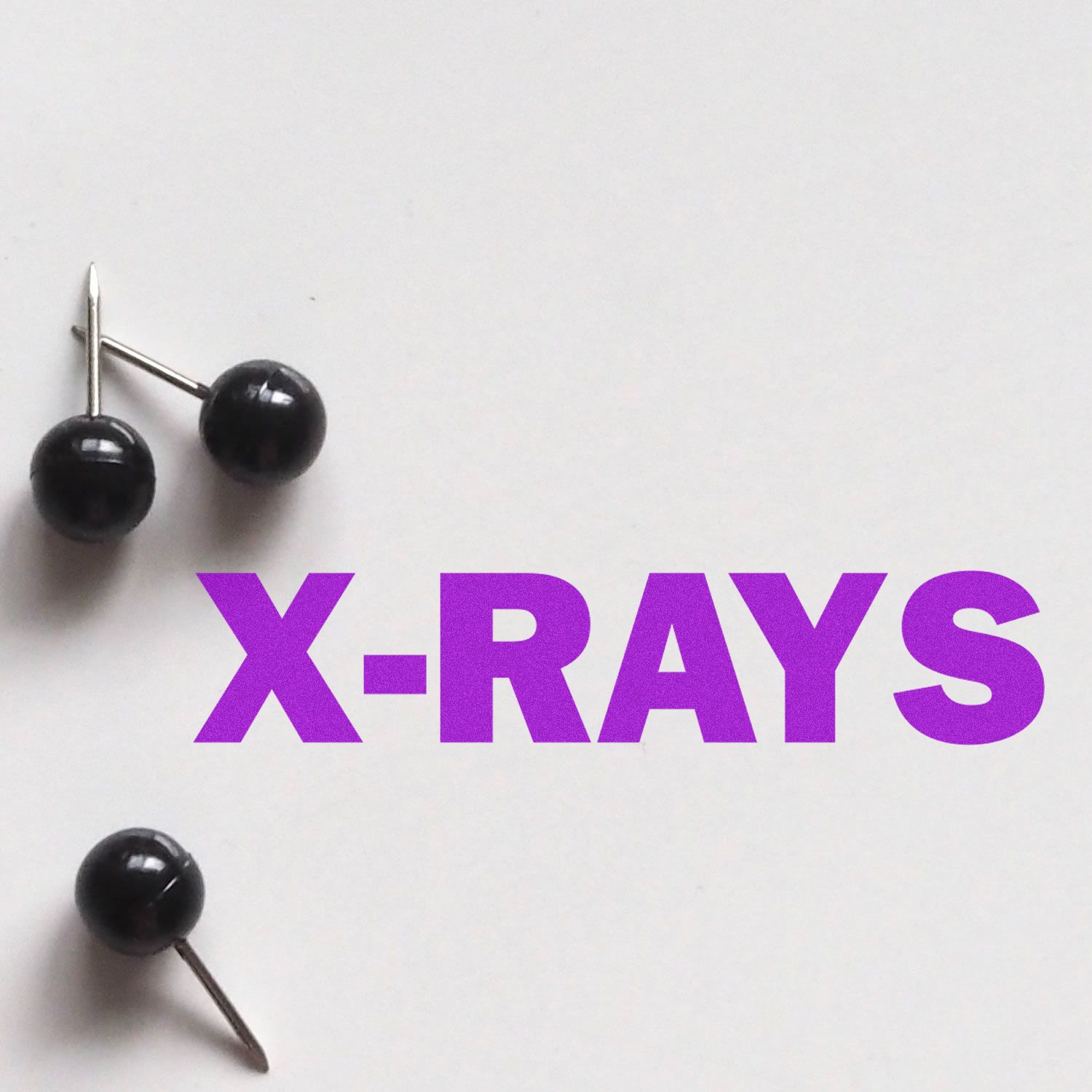 Large Self Inking X-Rays Stamp in use, displaying the word X-RAYS in bold purple letters on a white background with black push pins nearby.