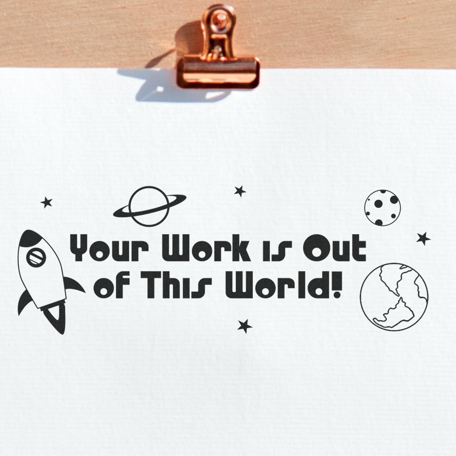 Your Work is Out of This World Rubber Stamp design with a rocket, planets, and stars on a white paper clipped to a wooden board.