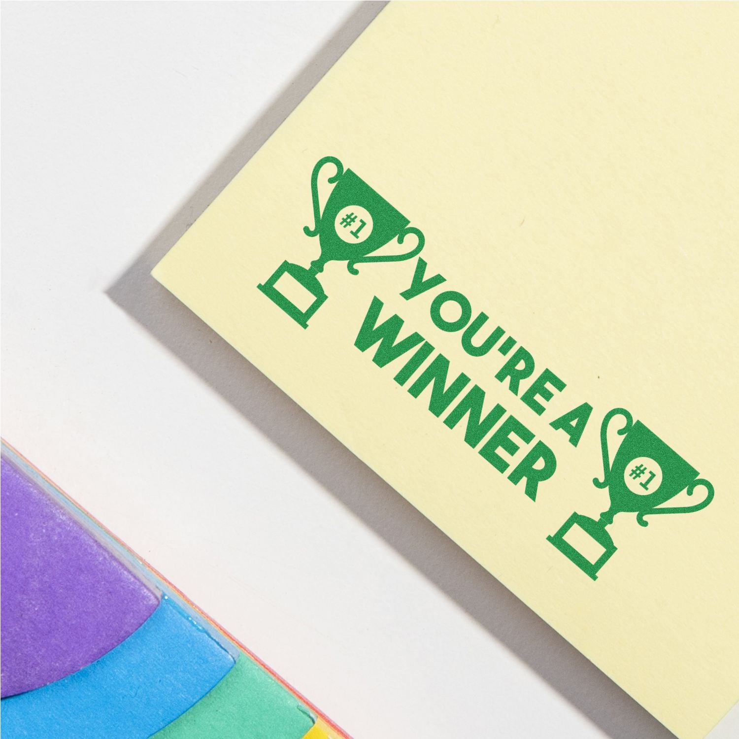 You're a Winner Rubber Stamp in green ink on yellow paper with trophy icons, next to colorful sticky notes.