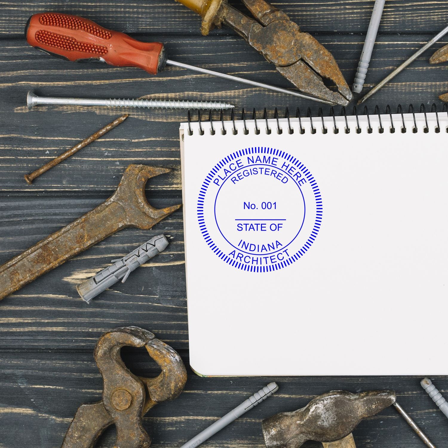 Indiana Architect Seal Stamp on a blank notepad surrounded by various rusty tools on a dark wooden surface.