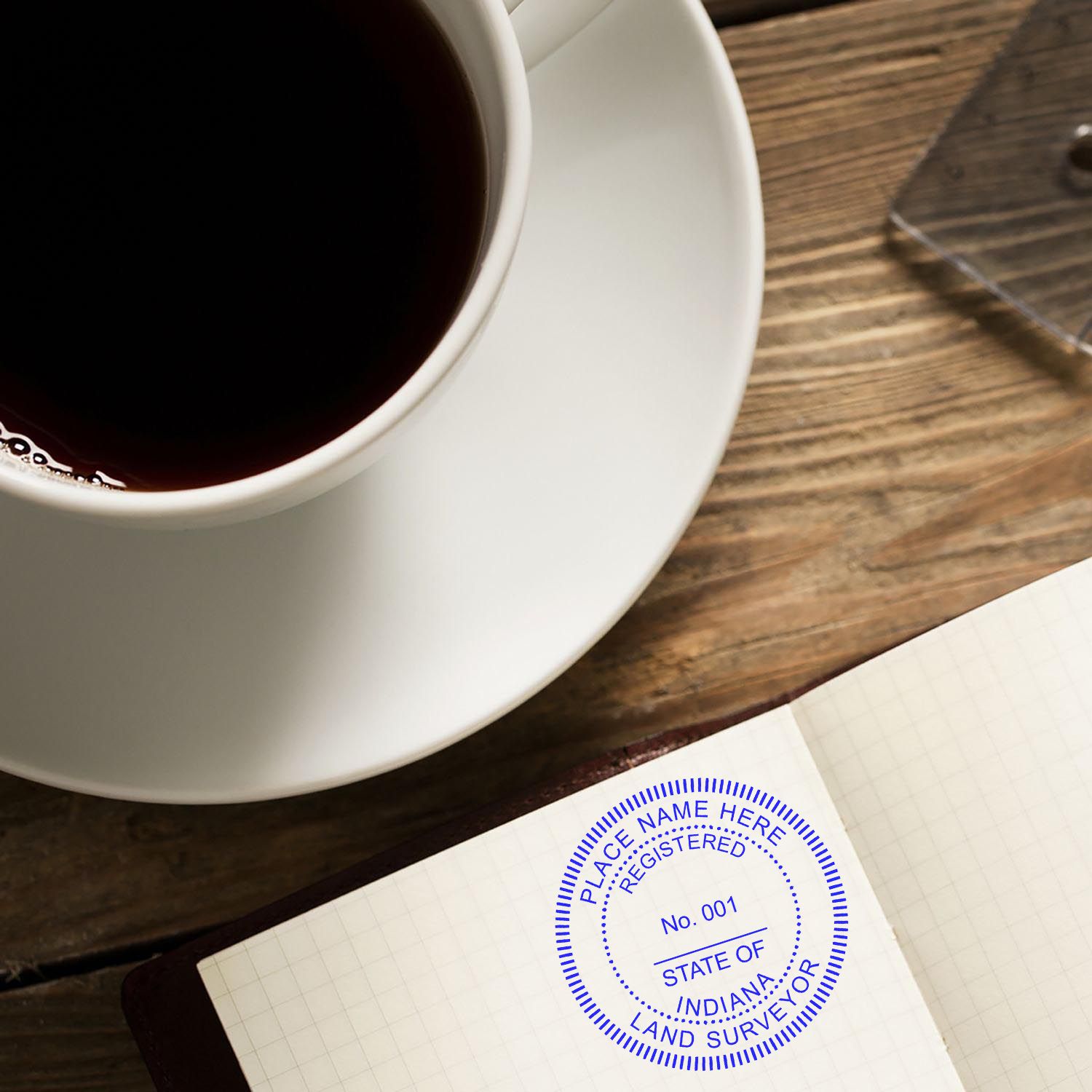 Indiana Land Surveyor Seal Stamp, IN PLS Stamp, imprinted on a notebook page next to a cup of coffee on a wooden table.