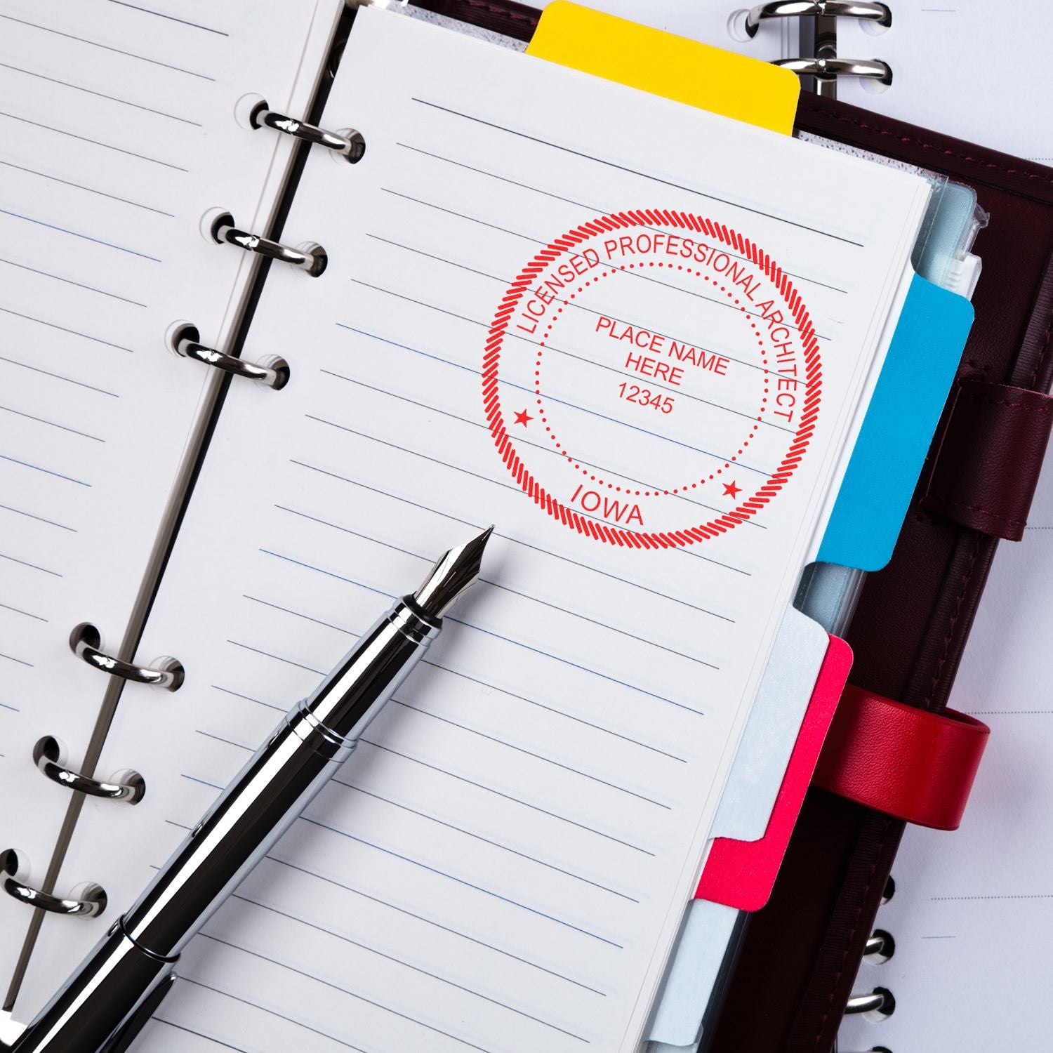 Iowa Architect Seal Stamp on a lined notebook page with a fountain pen and colorful tab dividers in a leather binder.