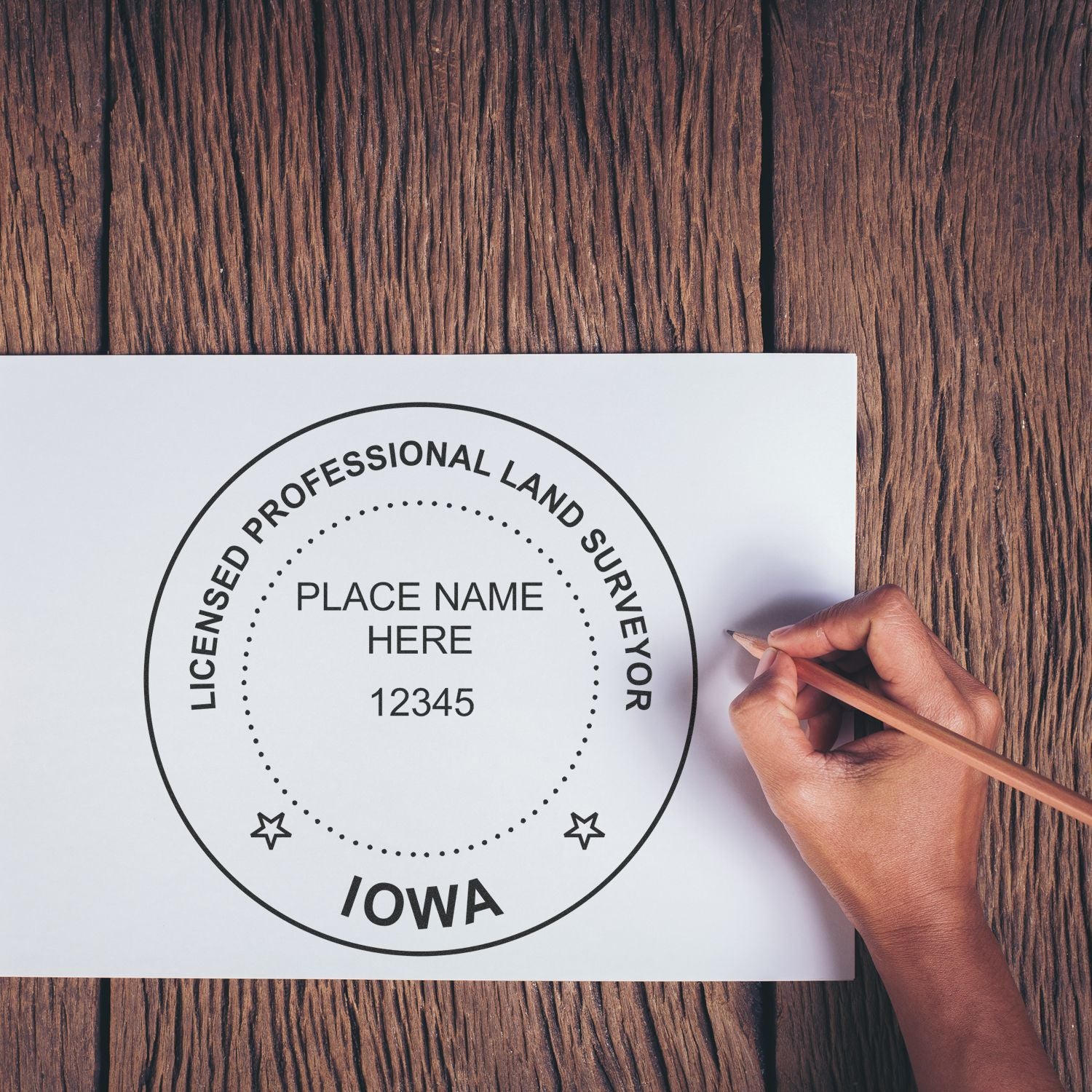 Hand using pencil to draw Iowa Land Surveyor Seal Stamp, IA PLS Stamp on white paper over wooden surface.