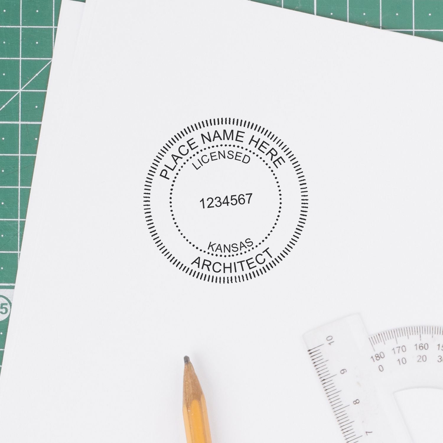 Kansas Architect Seal Stamp on white paper with pencil and ruler nearby on a green cutting mat.