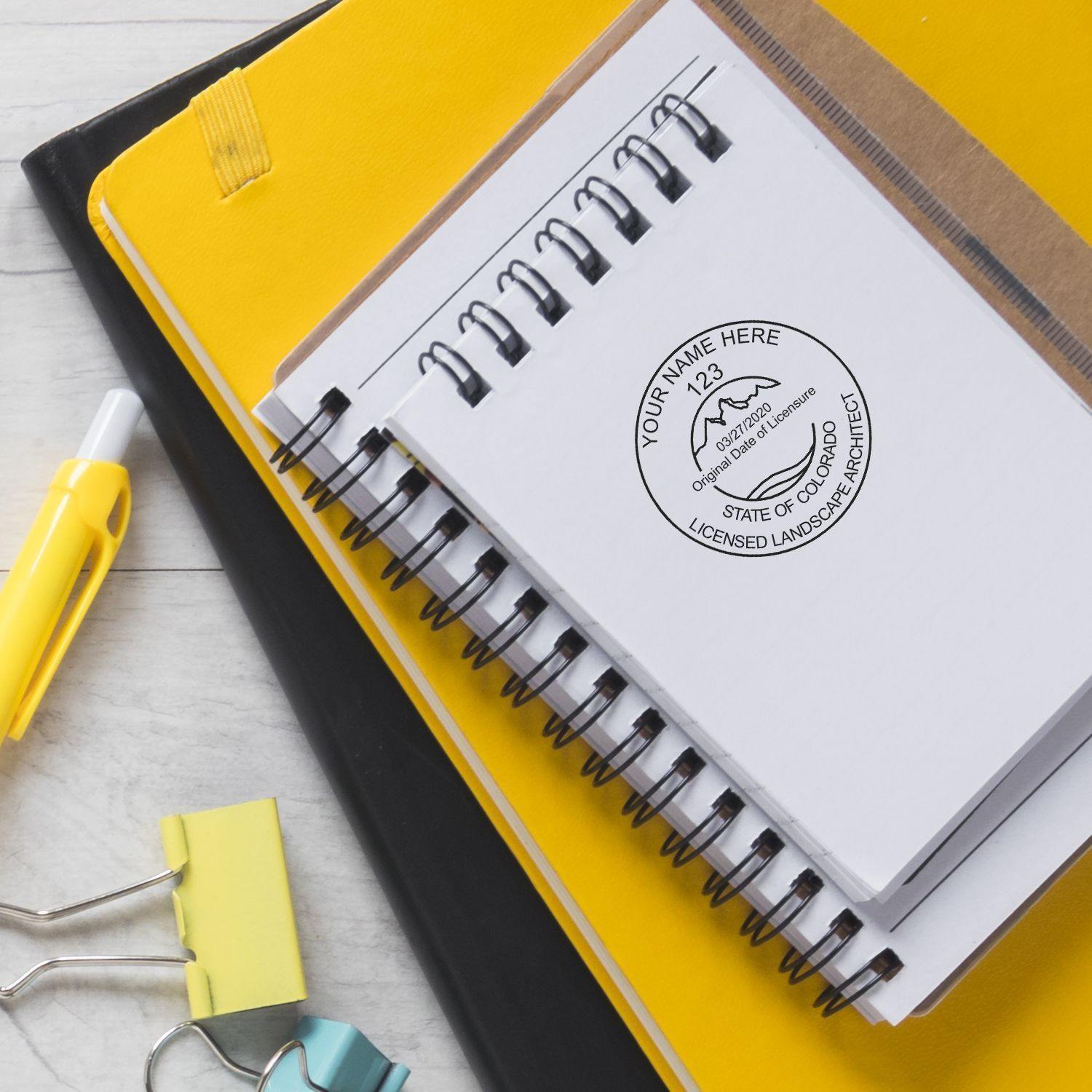 Xstamper Landscape Architect Pre-Inked Rubber Stamp of Seal used on a spiral notebook, surrounded by office supplies on a desk.