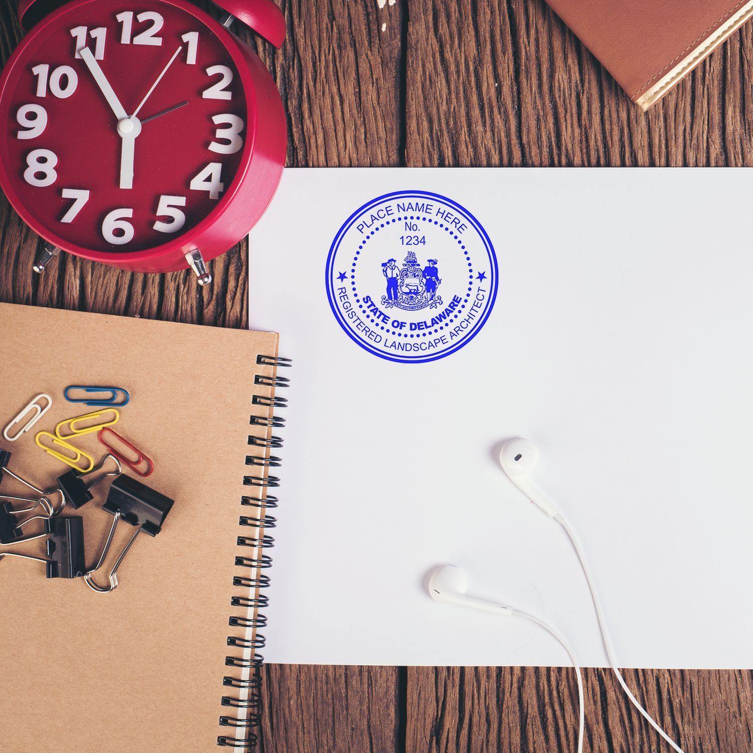 Landscape Architect MaxLight Pre Inked Rubber Stamp of Seal on white paper, surrounded by office supplies, a clock, and earphones.