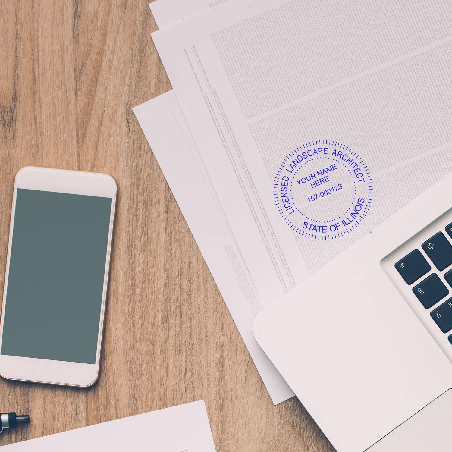 Landscape Architect MaxLight Pre Inked Rubber Stamp of Seal on a document beside a smartphone, pen, and laptop on a wooden desk.